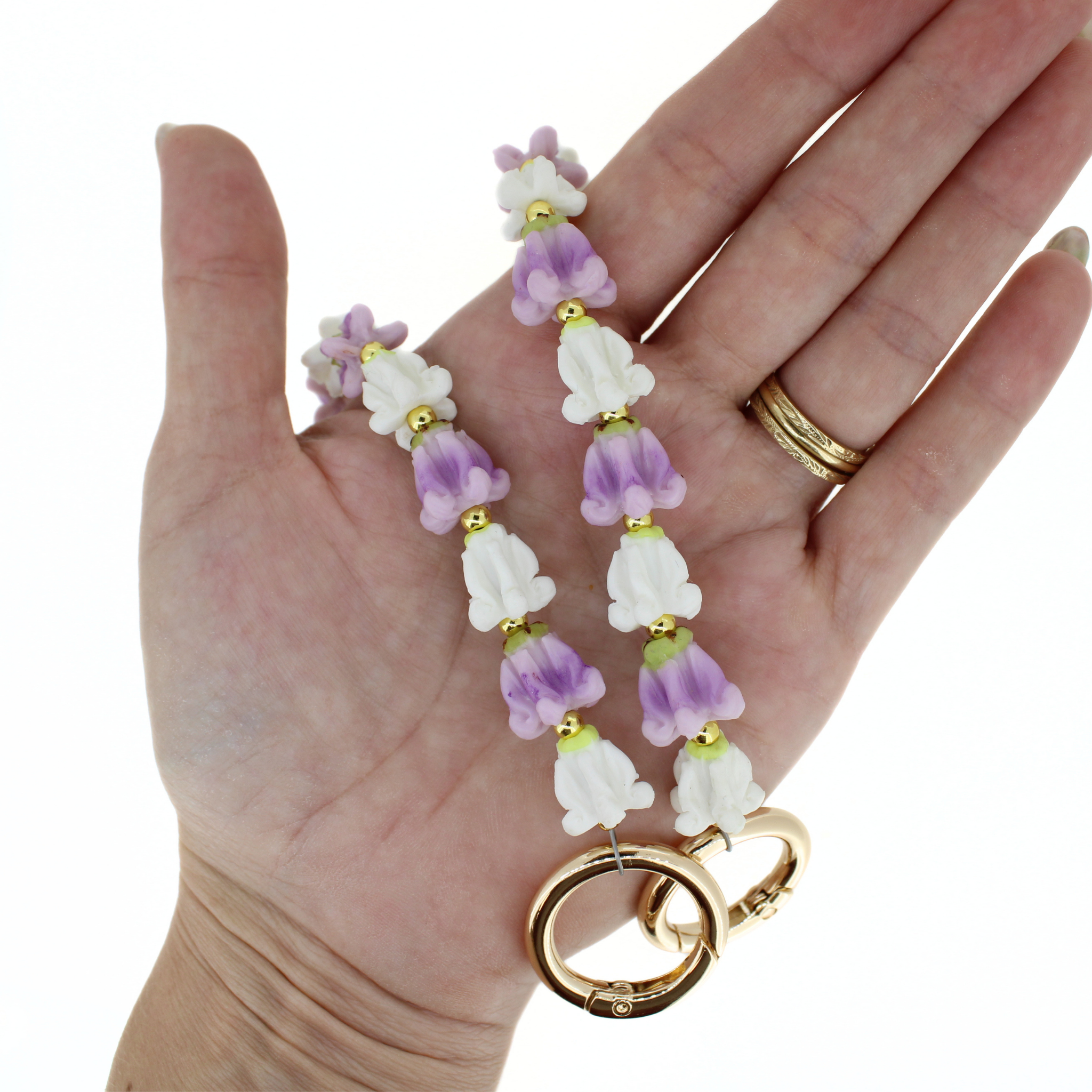 Floral bead lei on palm with white and lavender flowers, gold accents