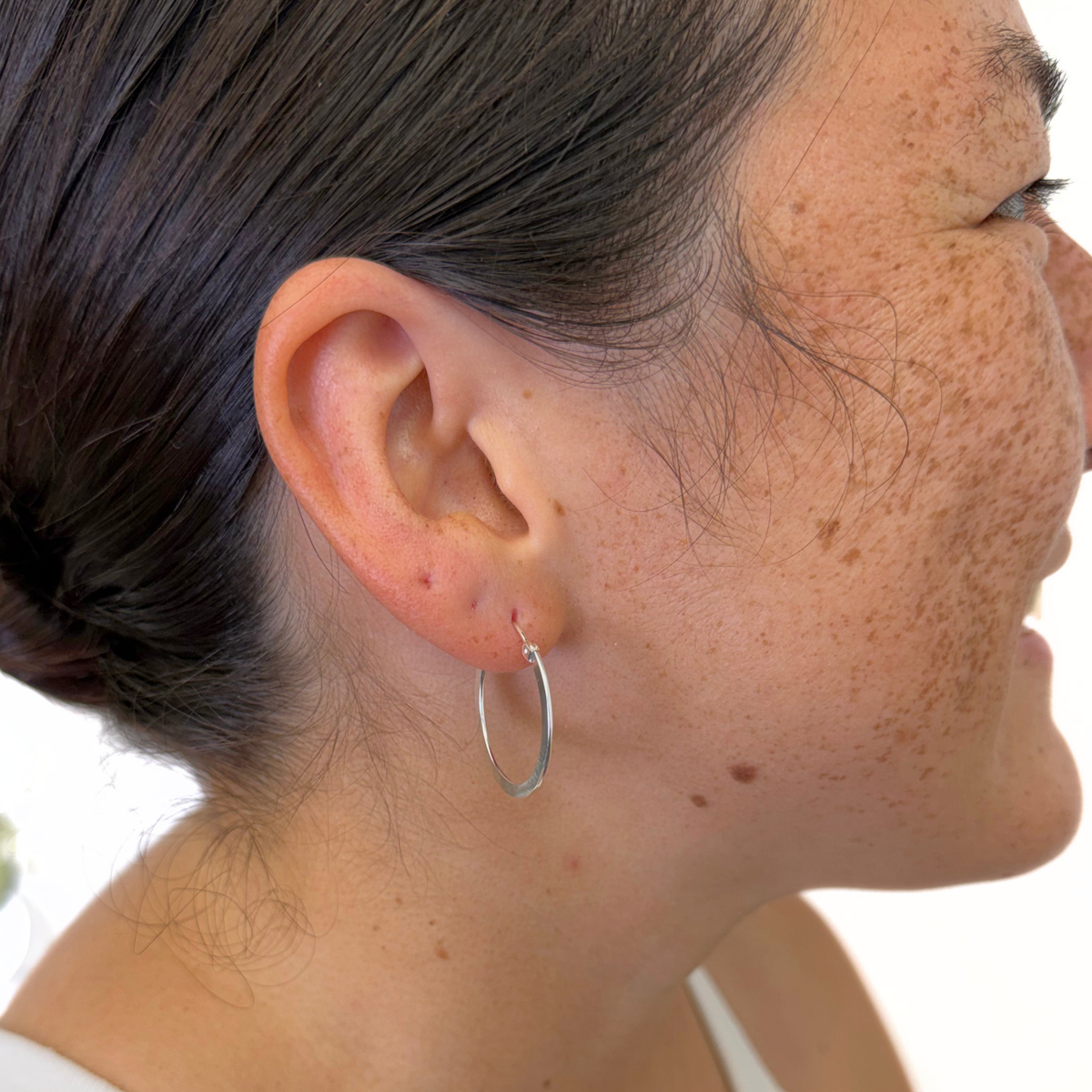 Sterling silver polished hoop earrings on a woman's ear for size reference