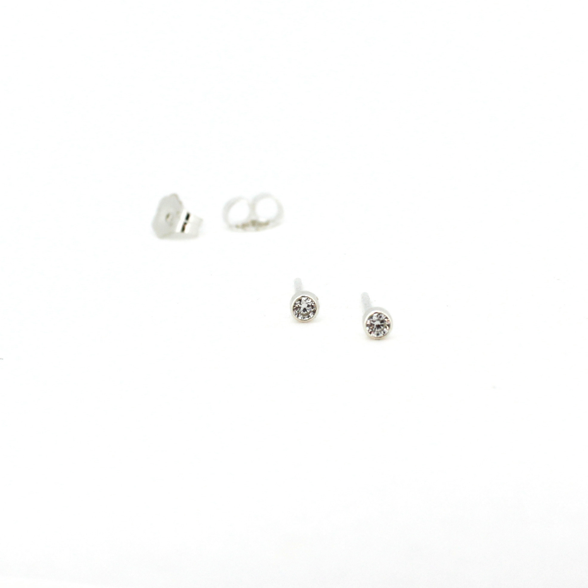 A pair of silver stud earrings with clear round gemstones, shown on a plain white background with one earring displaying its butterfly backing.