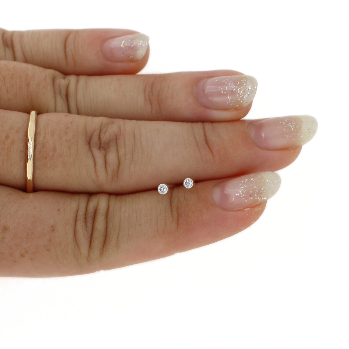A close-up of a hand holding a pair of small round stud earrings against a plain white background.