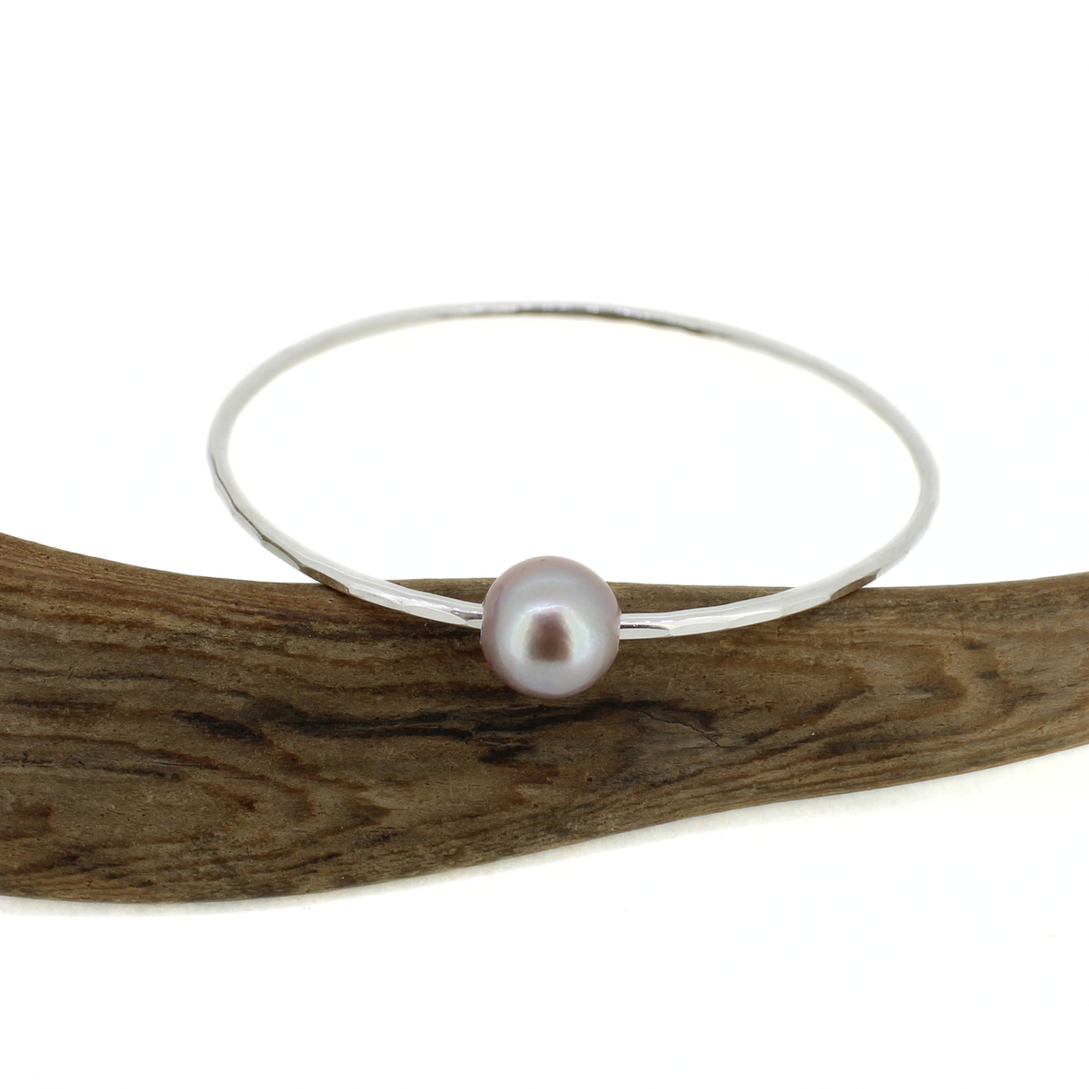 Silver bangle bracelet with hammered texture and a pink Edison pearl displayed on a piece of driftwood