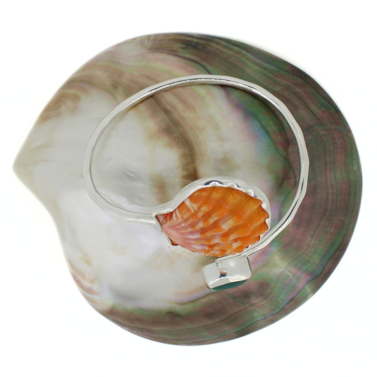 A silver bracelet featuring a small orange seashell mounted on the band, displayed against a large iridescent abalone shell on a white background.