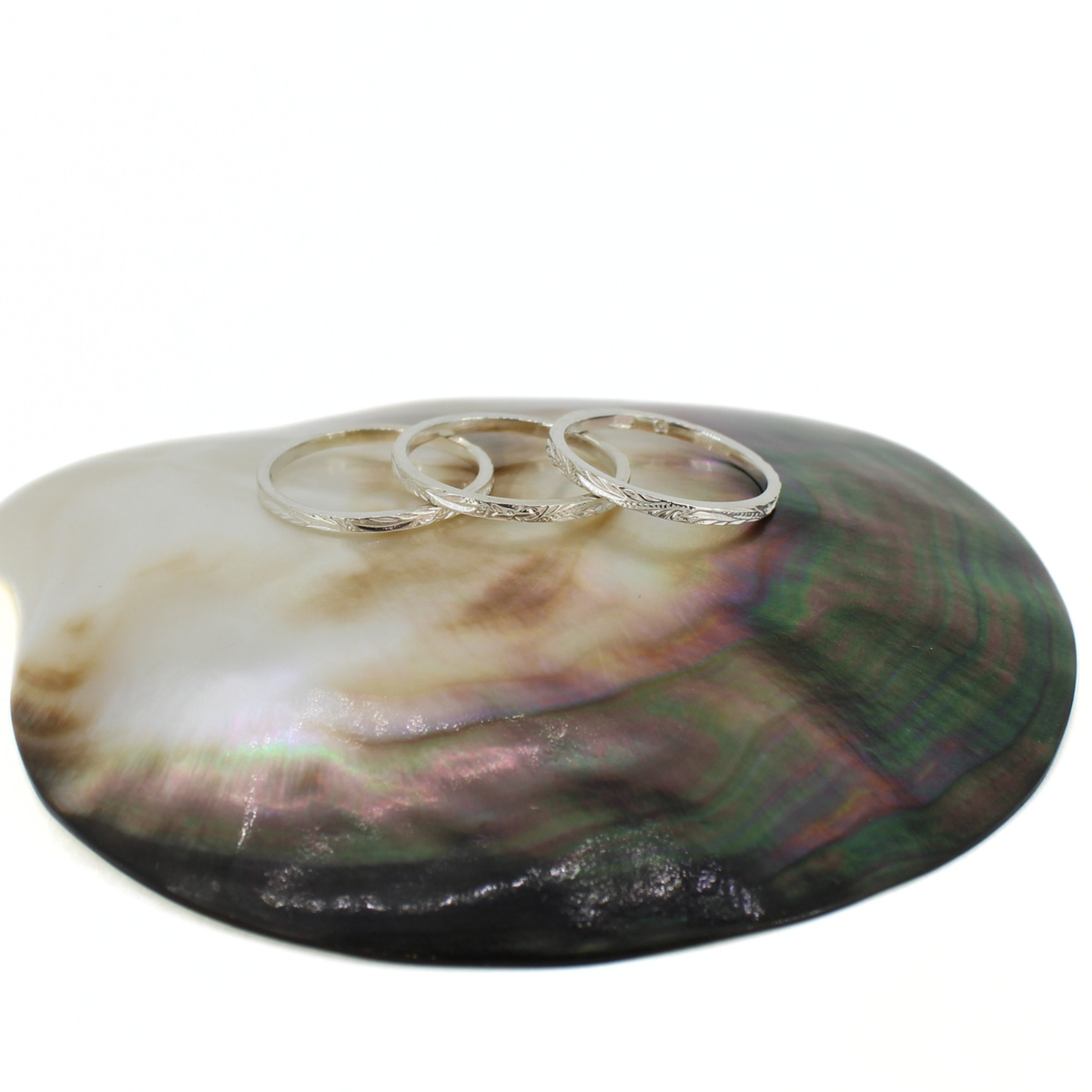 Three textured silver rings displayed on a large iridescent abalone shell tray against a white background.