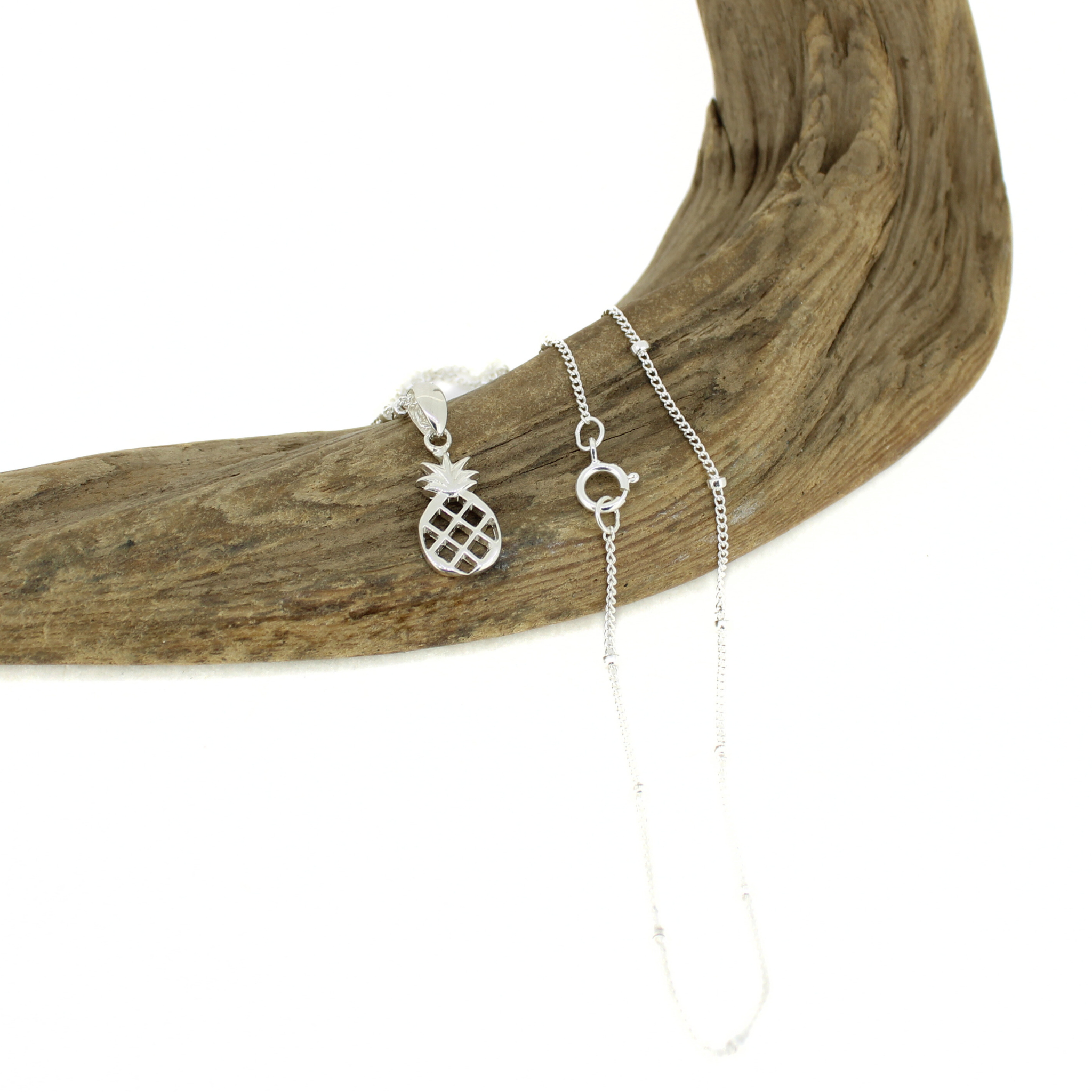 Silver pineapple charm necklace on a piece of driftwood with a white background