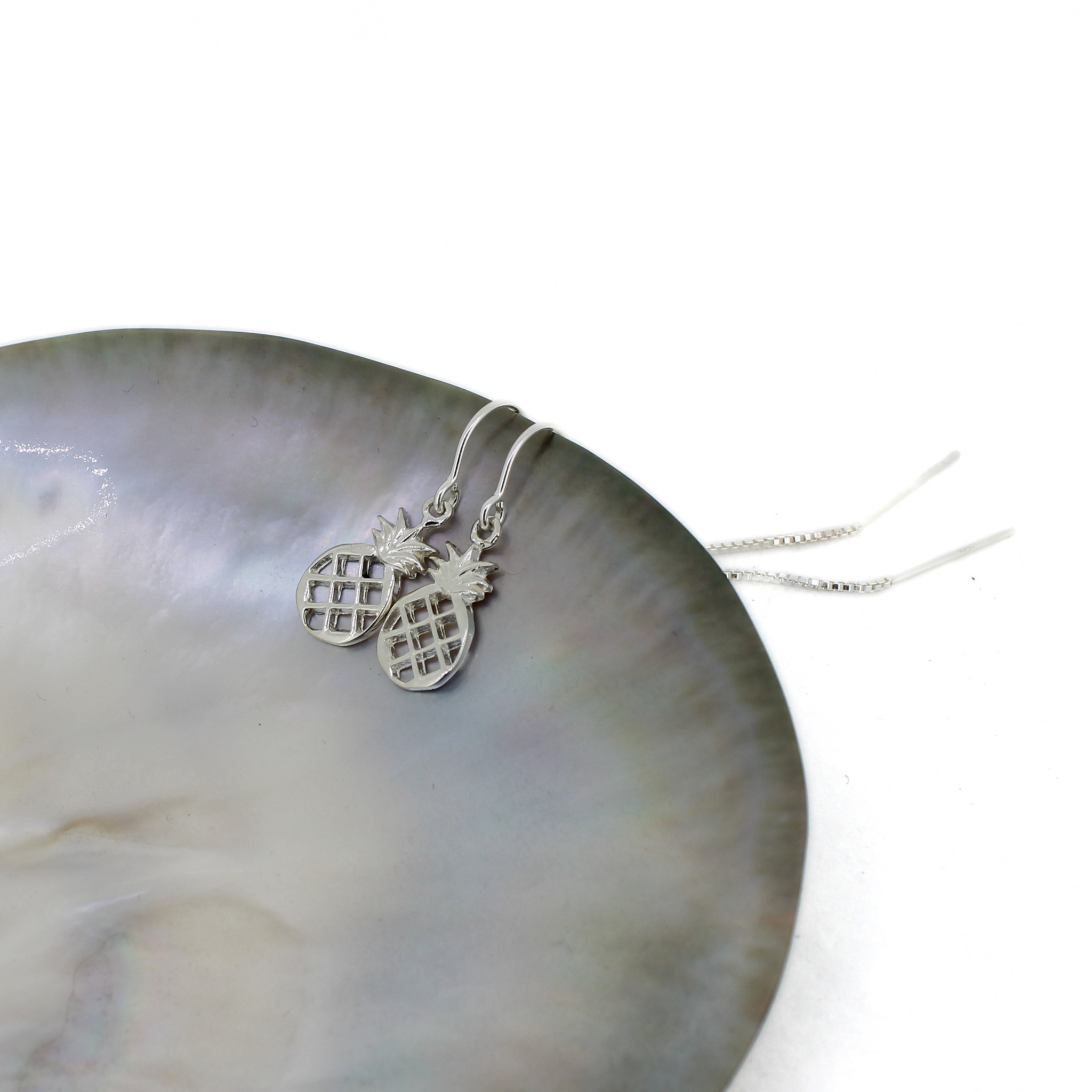 Brianne & Co. Sterling silver pineapple earrings on a shell with a white background