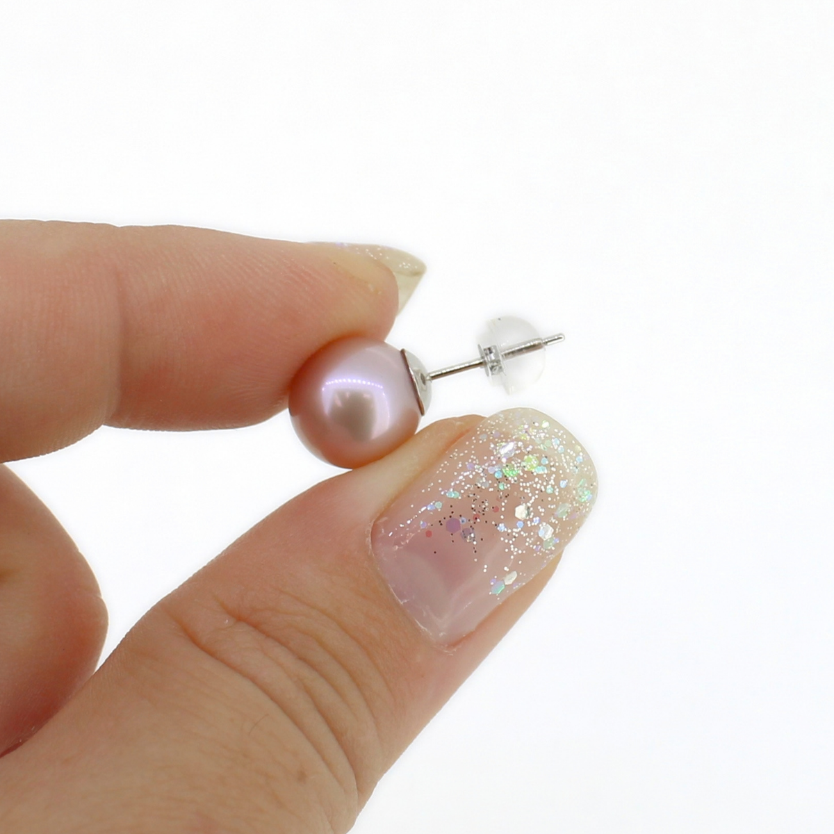 A close-up of a hand holding a single pearl stud earring with a silver post and clear backing against a white background.