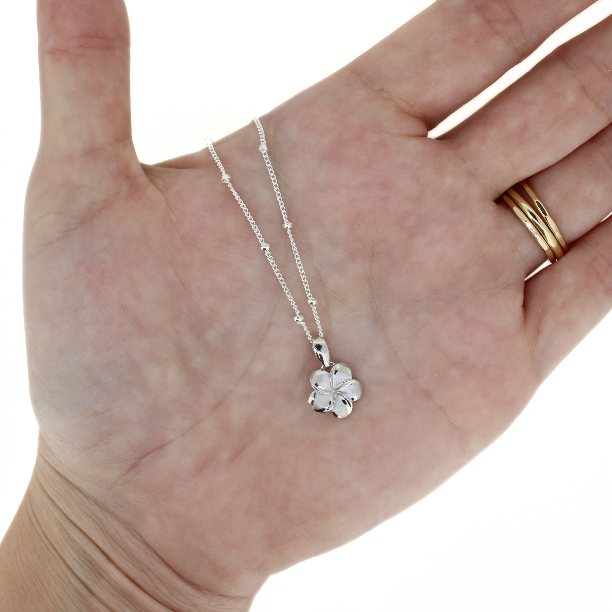 Brianne & Co. small sterling silver plumeria pendant on hand for size reference