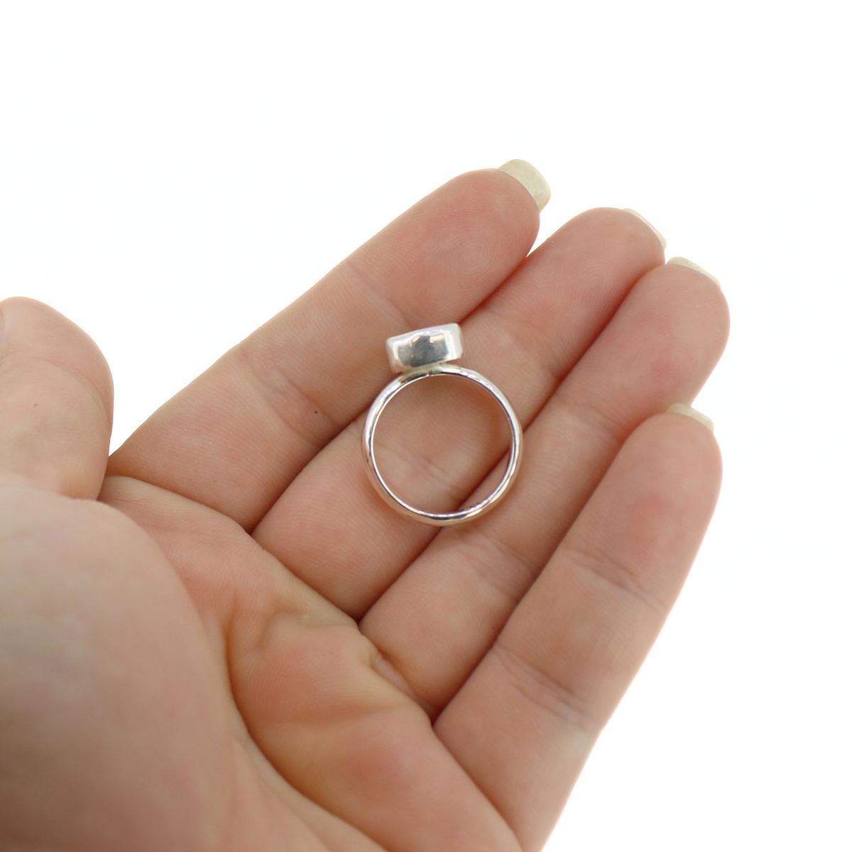 A silver ring with a flat, rectangular bezel-set top held in the palm of a hand against a plain white background.