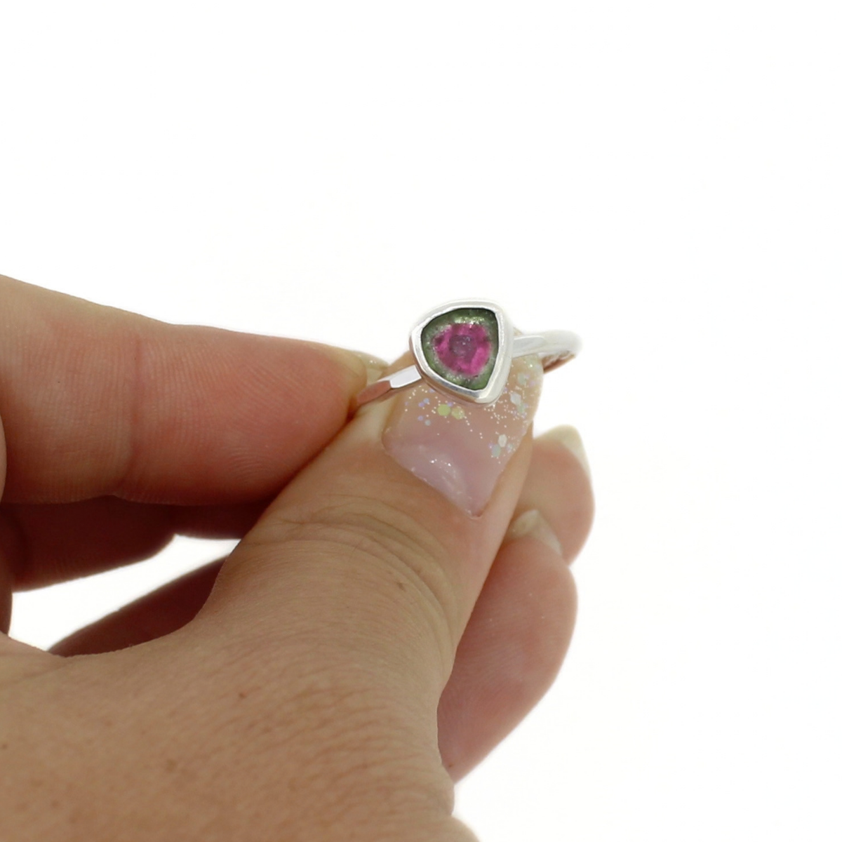 A silver ring with a triangular-shaped pink and green tourmaline gemstone held between fingers against a plain white background.