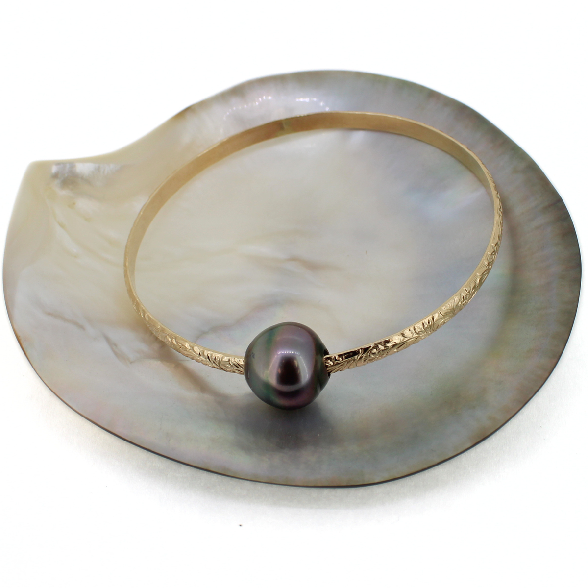 Brianne & co. 14k gold fill Hawaiian heirloom style bangle bracelet with large Tahitian pearl displayed on a shell