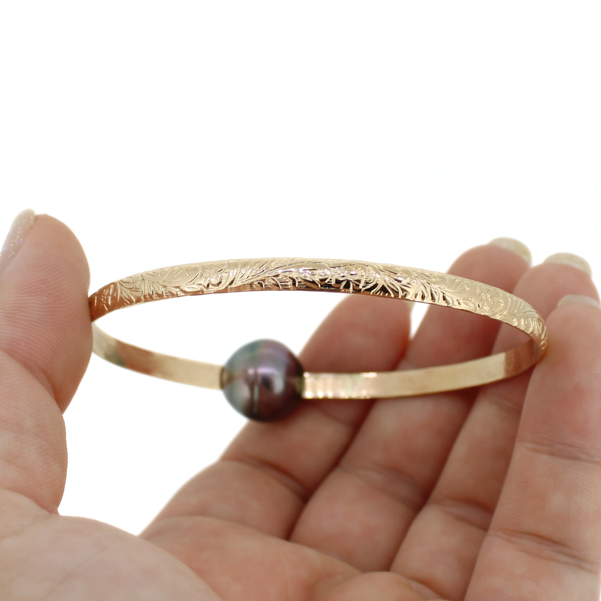 Gold pearl bangle bracelet with a floral Hawaiian heirloom style design held in hand against a white background