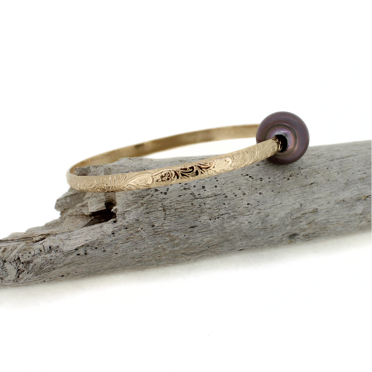 Gold fill bangle bracelet with floral printed design and a large Tahitian pearl displayed on a piece of drift wood