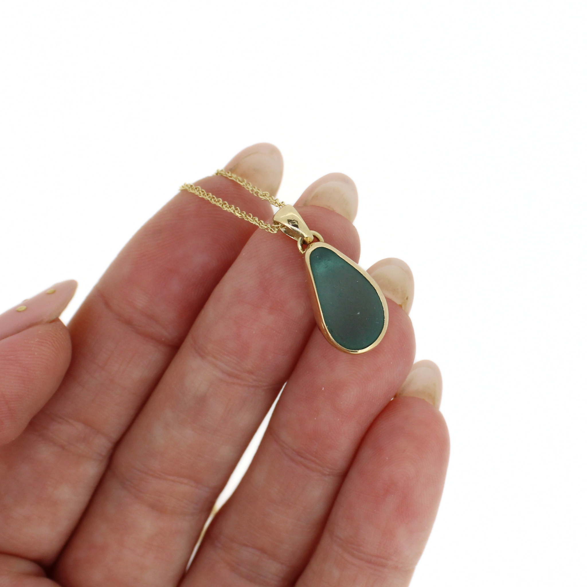 Gold sea glass pendant necklace with teardrop blue stone, close-up