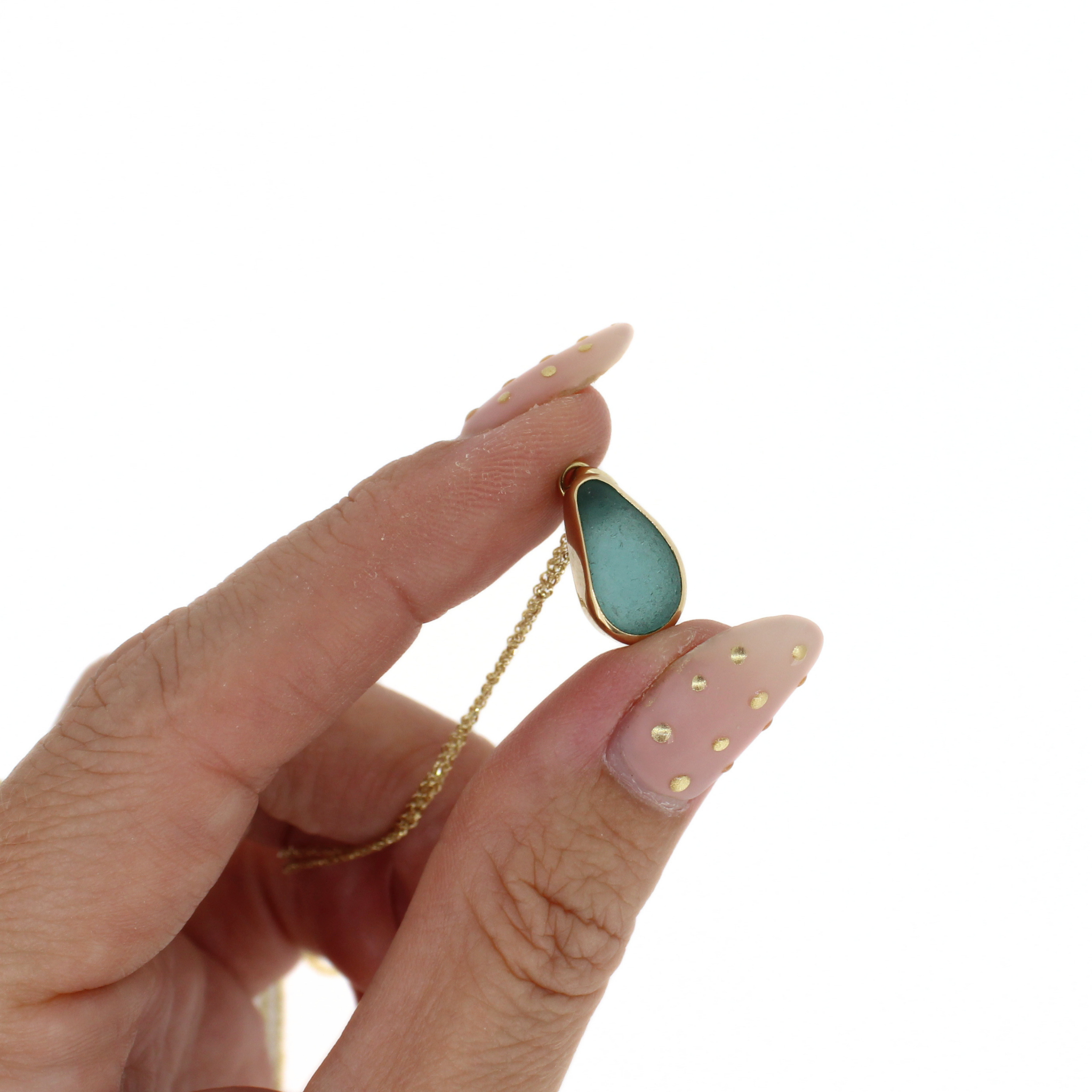 Gold chain necklace with teardrop blue sea glass charm, close-up on hand