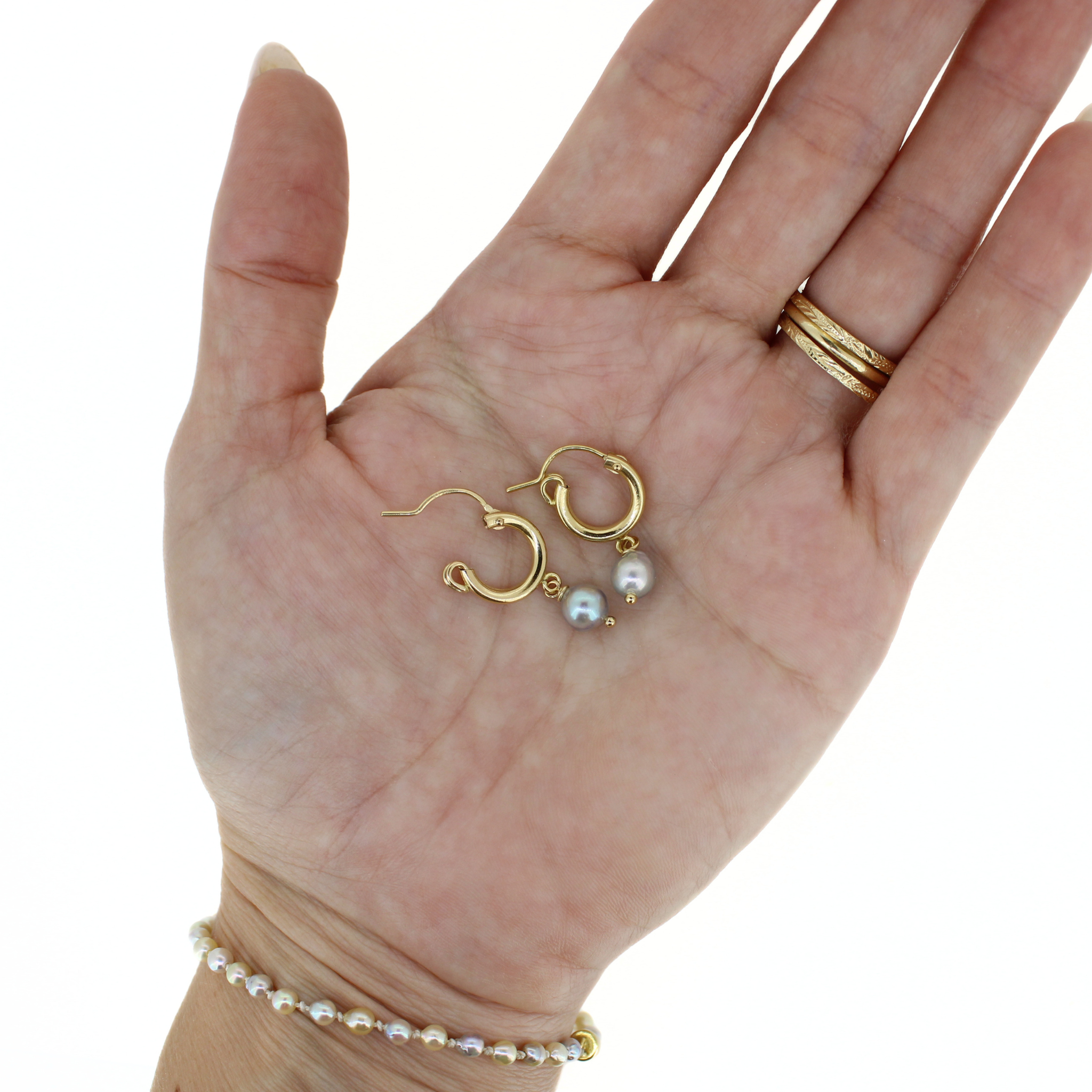 Gold hoop earrings with blue Akoya pearl drops resting in open palm