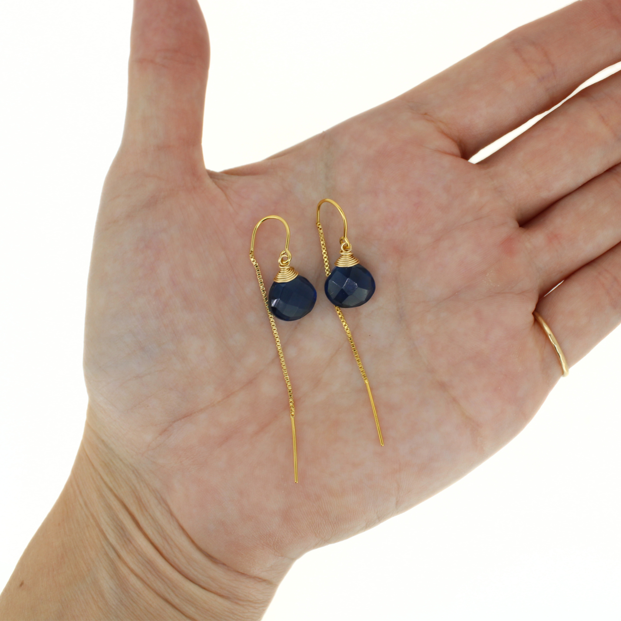 Gold-tone threader earrings with blue faceted drops, shown on a hand