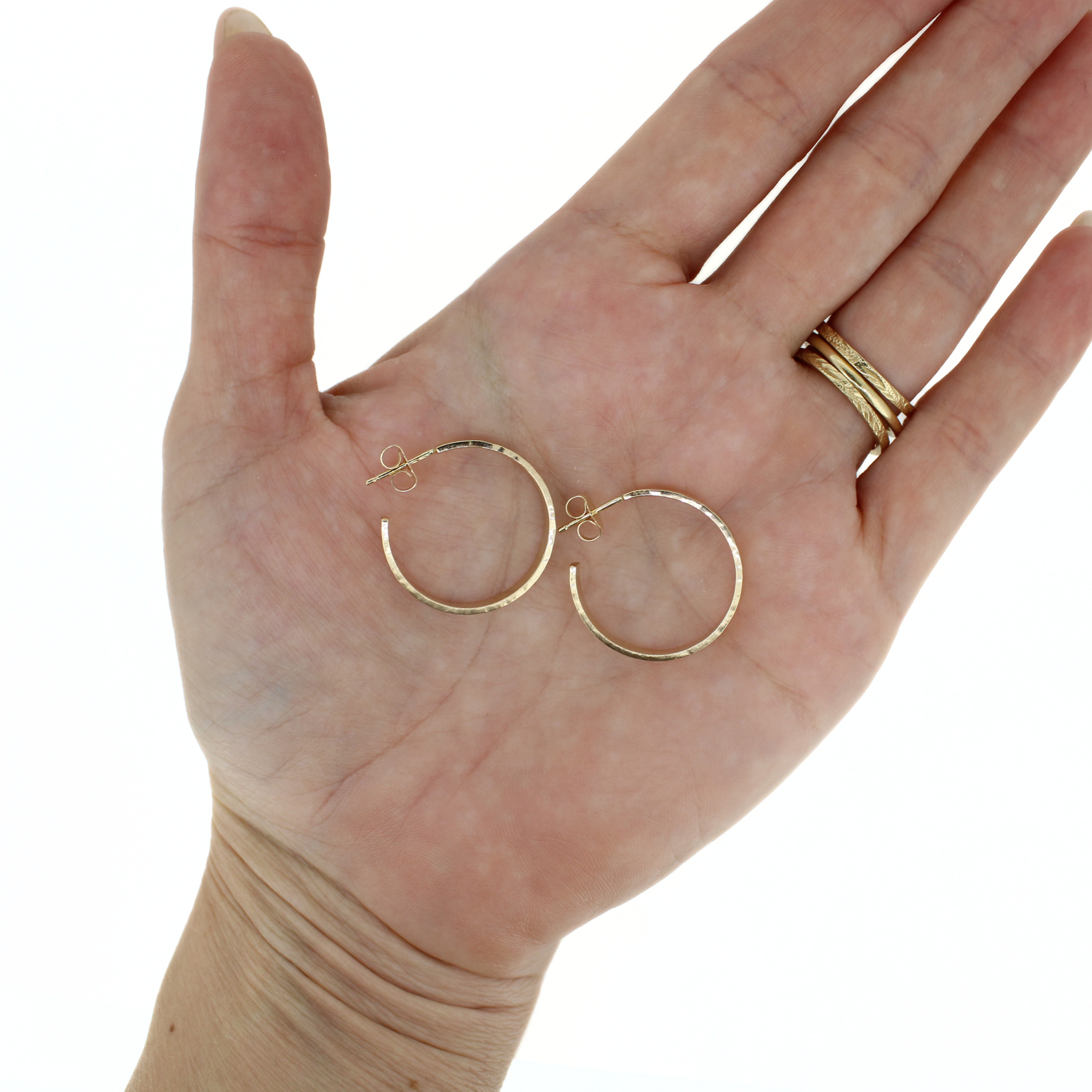 A pair of small gold hoop earrings displayed on an open hand, against a plain white background.