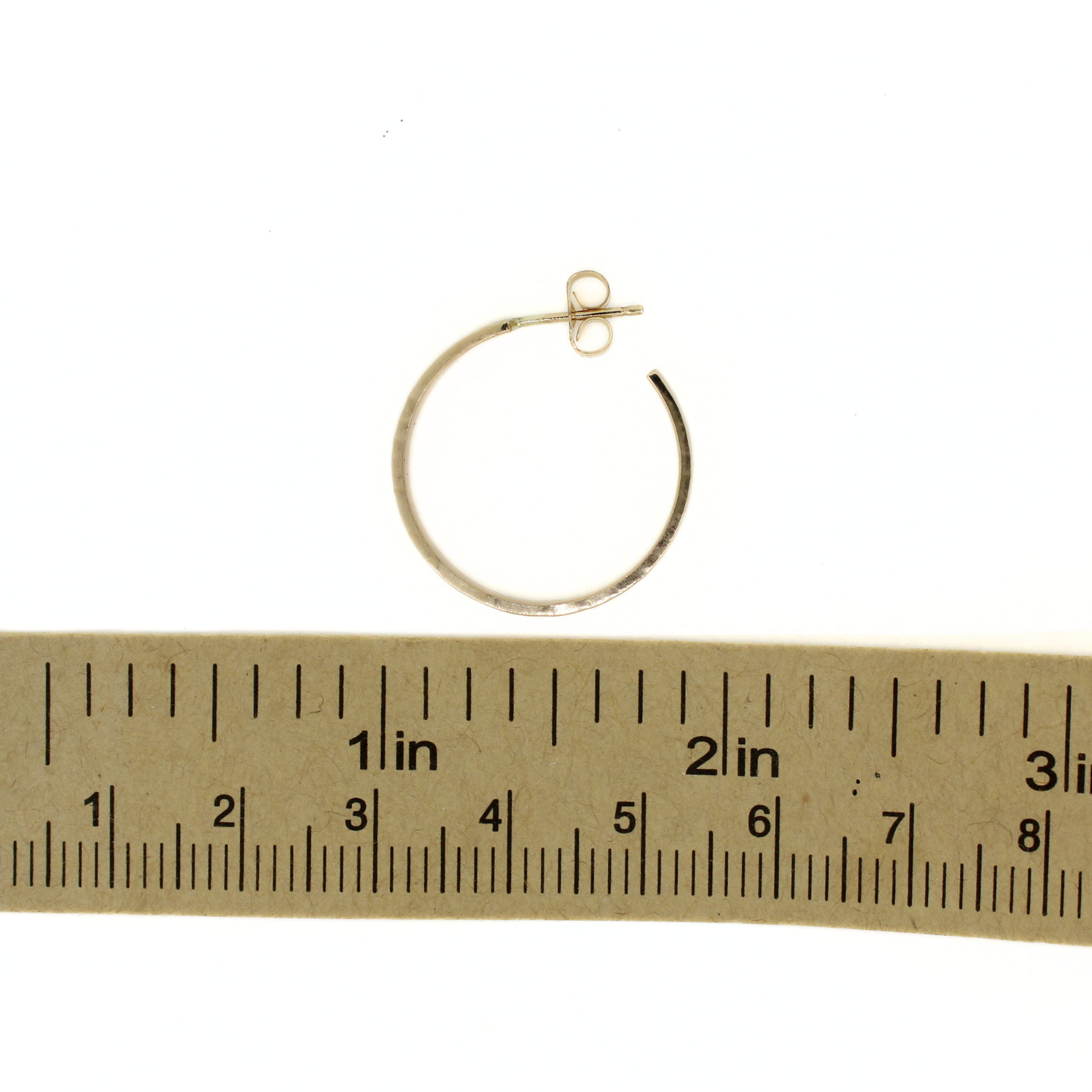 A small gold hoop earring with a post and butterfly back, shown above a ruler for scale on a white background.