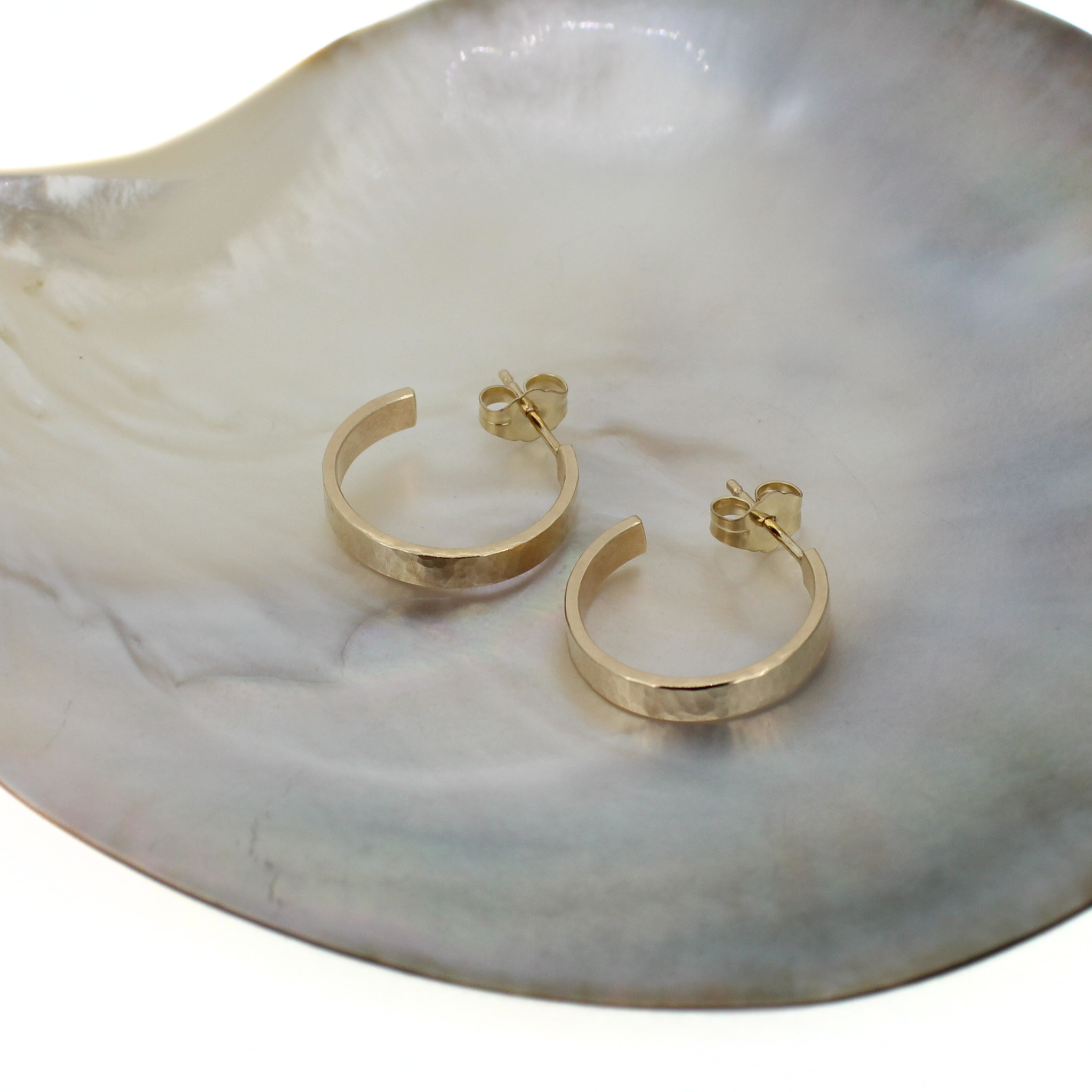 A pair of gold hoop earrings with a hammered texture, displayed on a white and gray marbled shell dish.