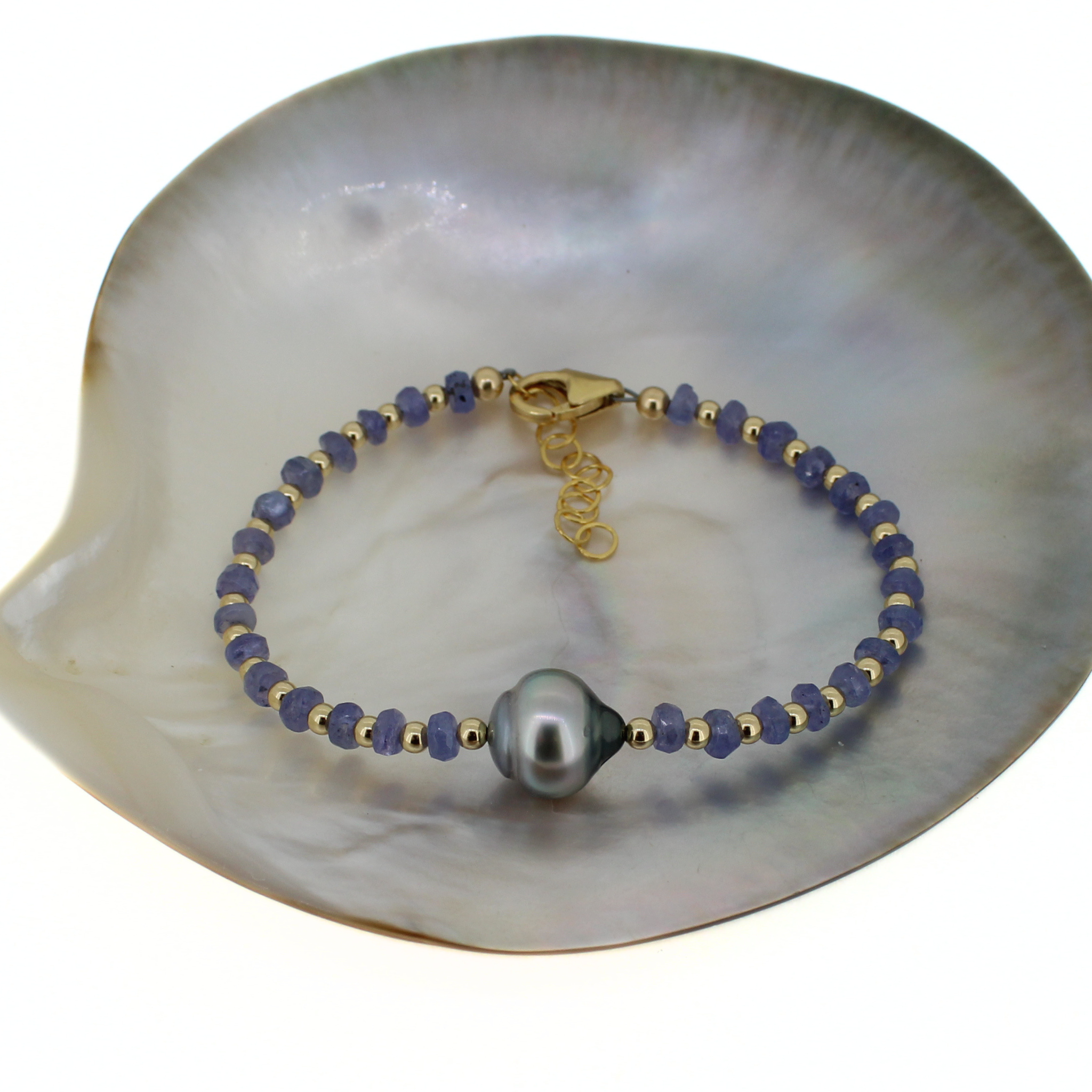 Gold bracelet on shell: dark blue beads and three gray baroque pearls with dangling chain.