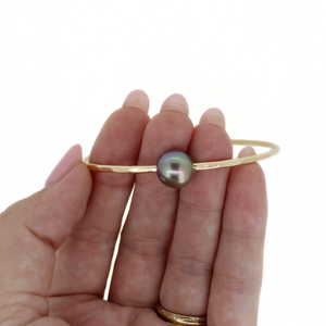 Gold bracelet with a pearl held in a hand on a white background