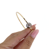 Hand holding a gold bangle with a pearl on a white background
