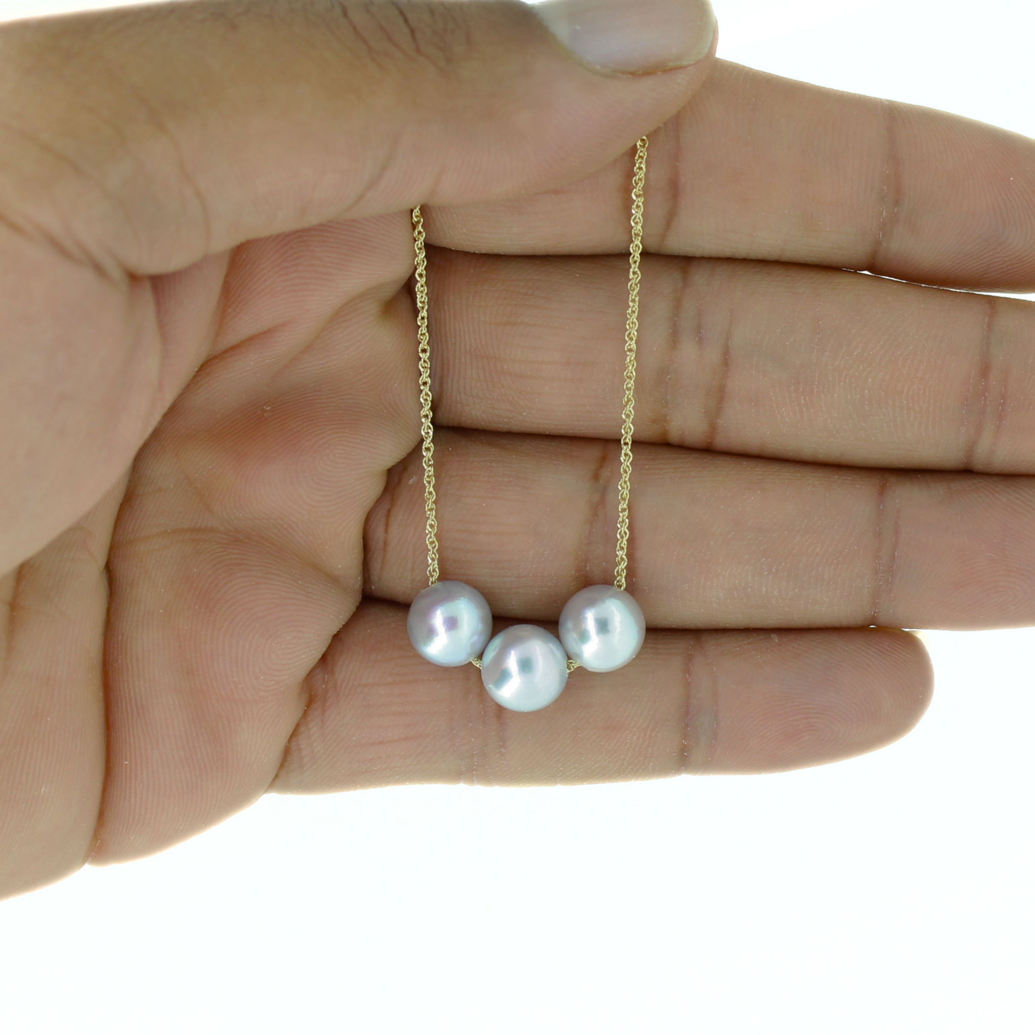 A close-up of a hand holding a delicate gold chain necklace with three small pearls, shown against a plain white background.