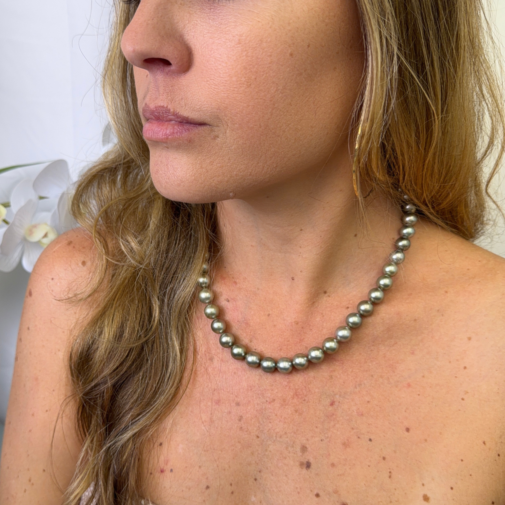 A close-up of a woman wearing a single-strand necklace made of round Tahitian pearls individually hand knotted.