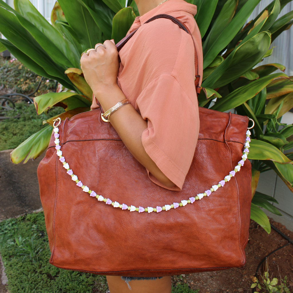Person holding a brown leather handbag with a decorative flower purse lei