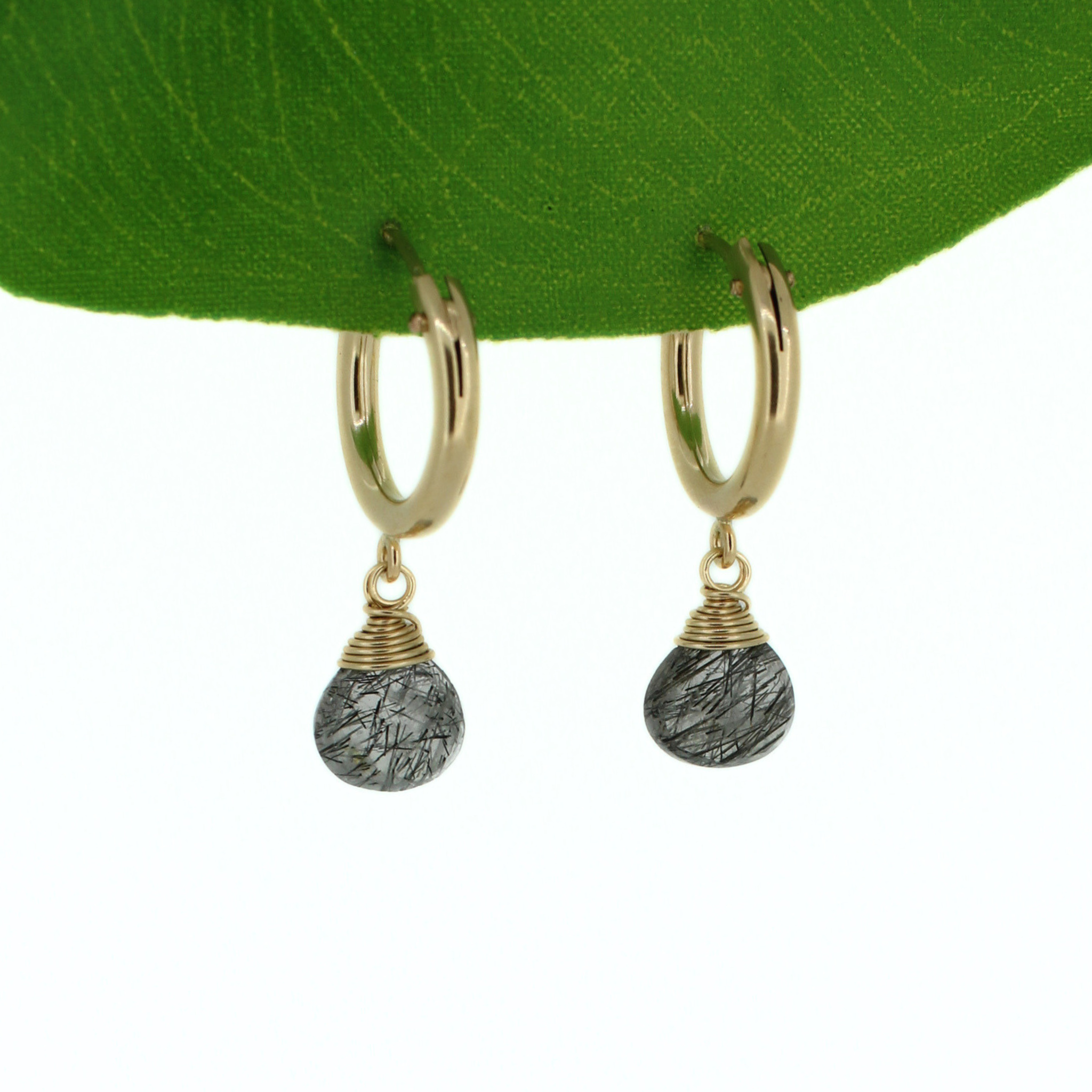 A pair of gold hoop earrings with teardrop-shaped rutile quartz gemstones, displayed against a green leaf on a white background. Handmade by Brianne & Co. in Kauai, Hawaii 