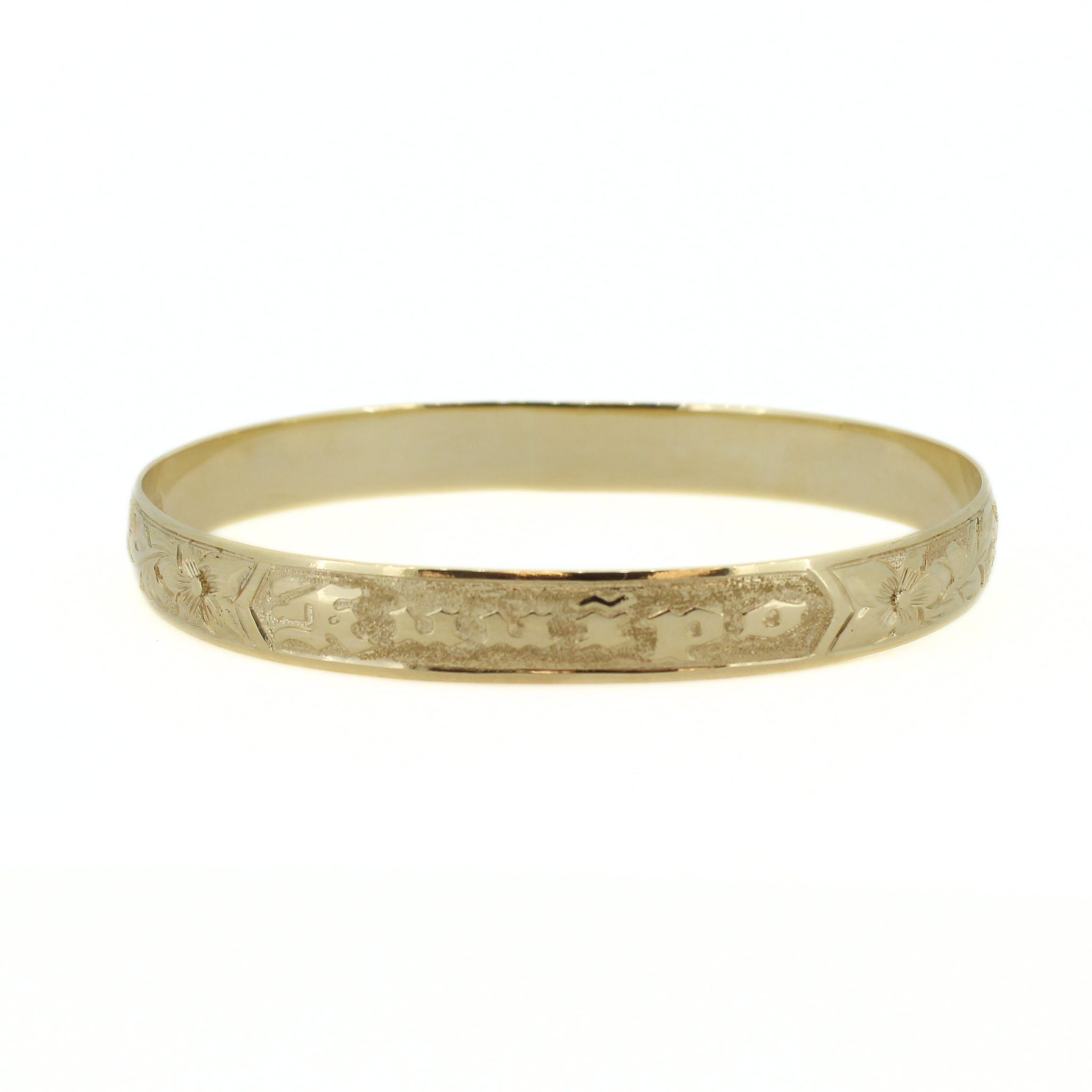 Gold bangle lying flat, with engraved row of tropical motifs along the center