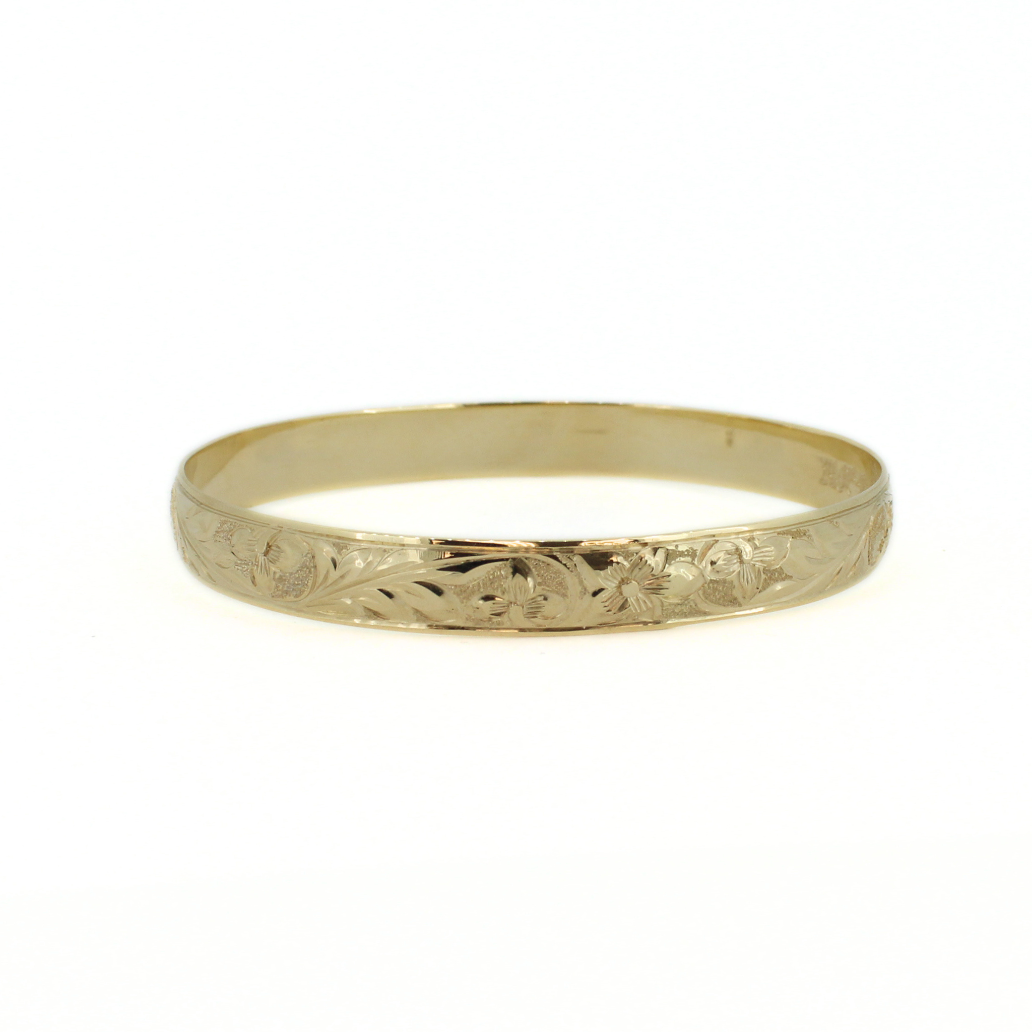 Gold bangle with detailed engraved pattern on the front, lying flat
