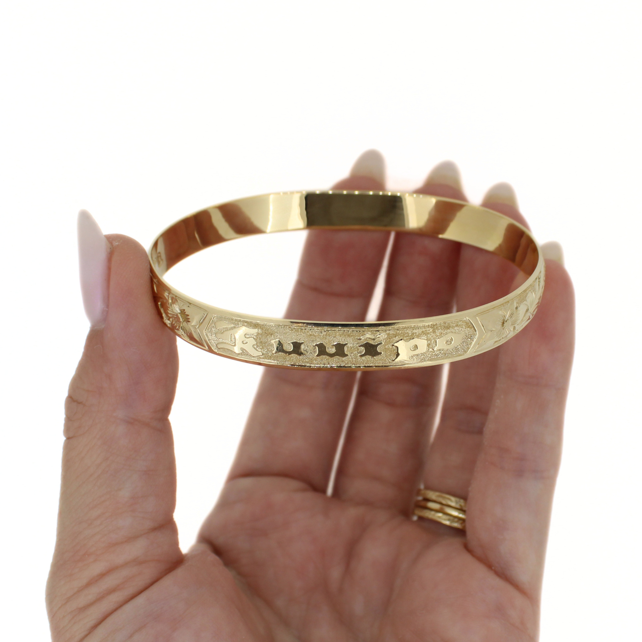 Gold bangle shown from inside edge, with engraved row of tropical motifs