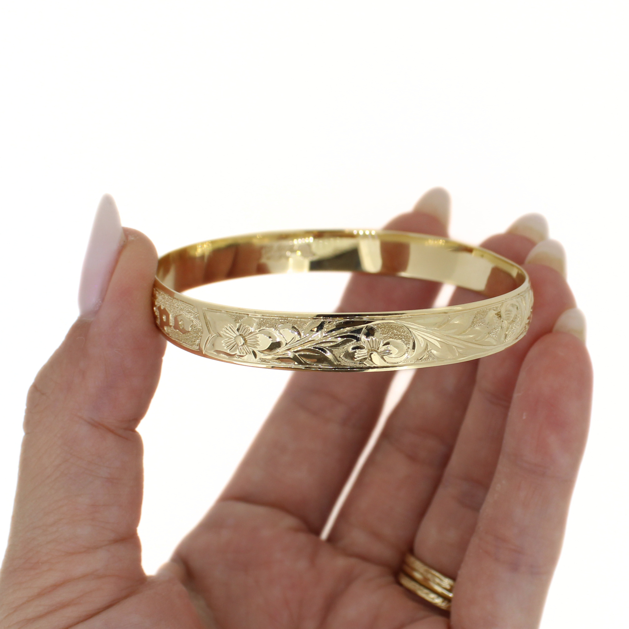 Gold bangle on palm, close view of engraved floral and wave motifs