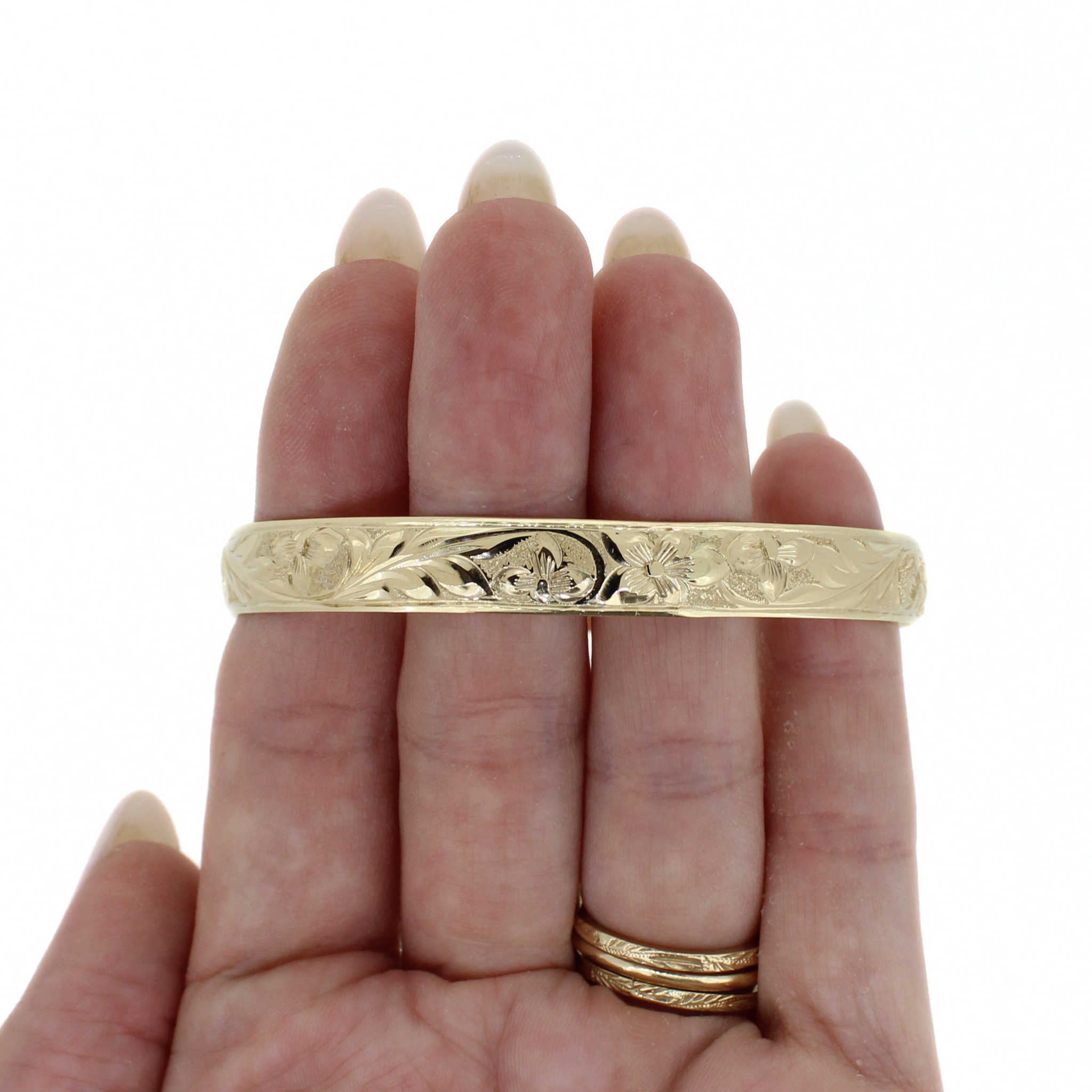 Gold bangle on hand, featuring etched floral and wave pattern around the band