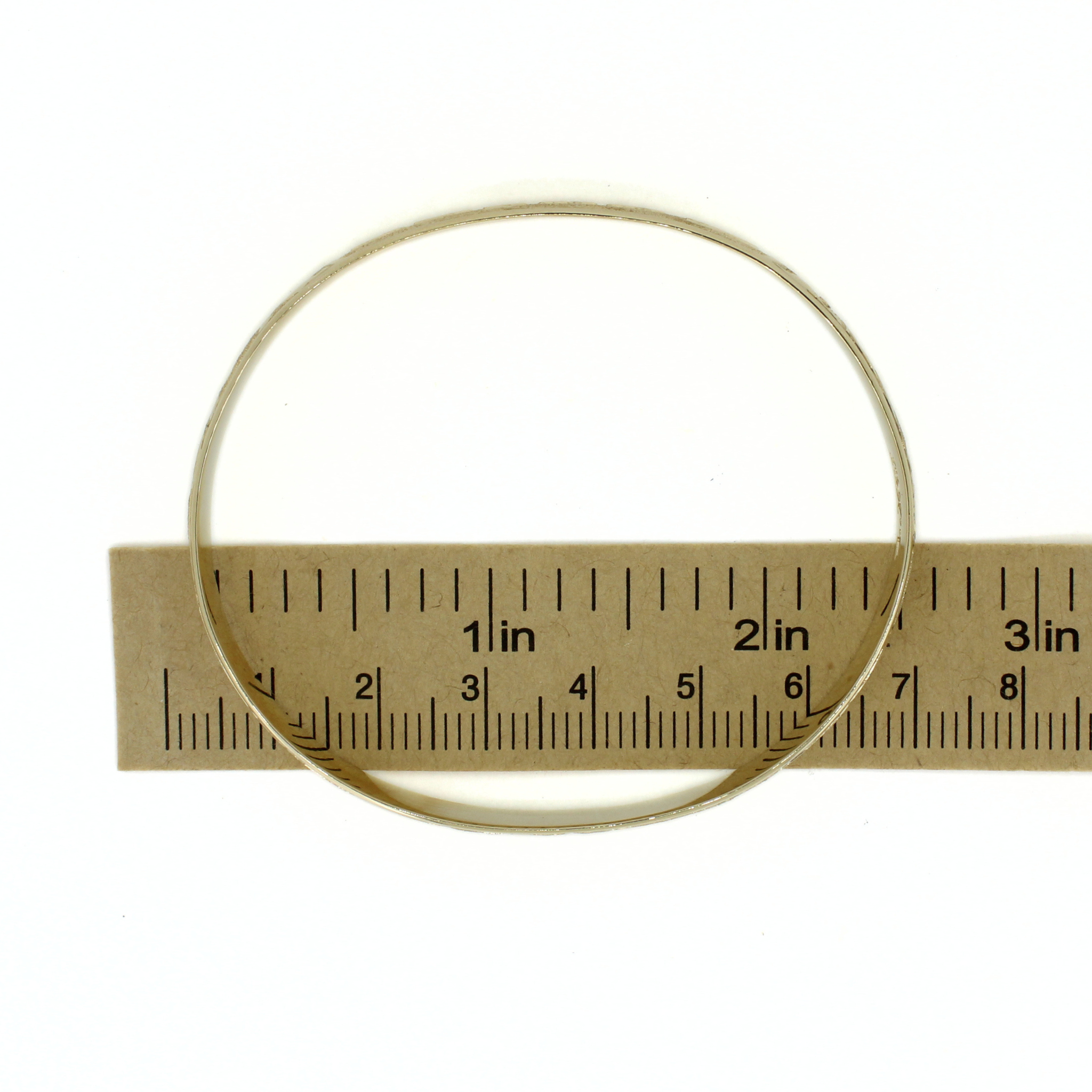 Gold bangle with engraved tropical motifs, sized with a ruler for reference