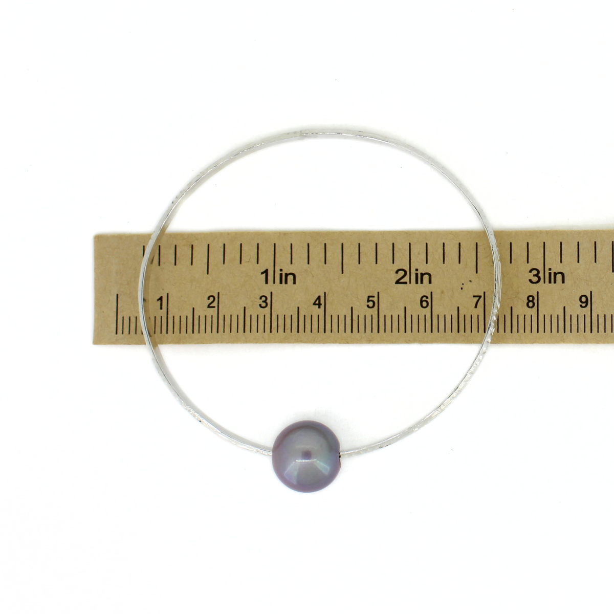 Sterling silver oval bangle bracelet over a ruler for size reference