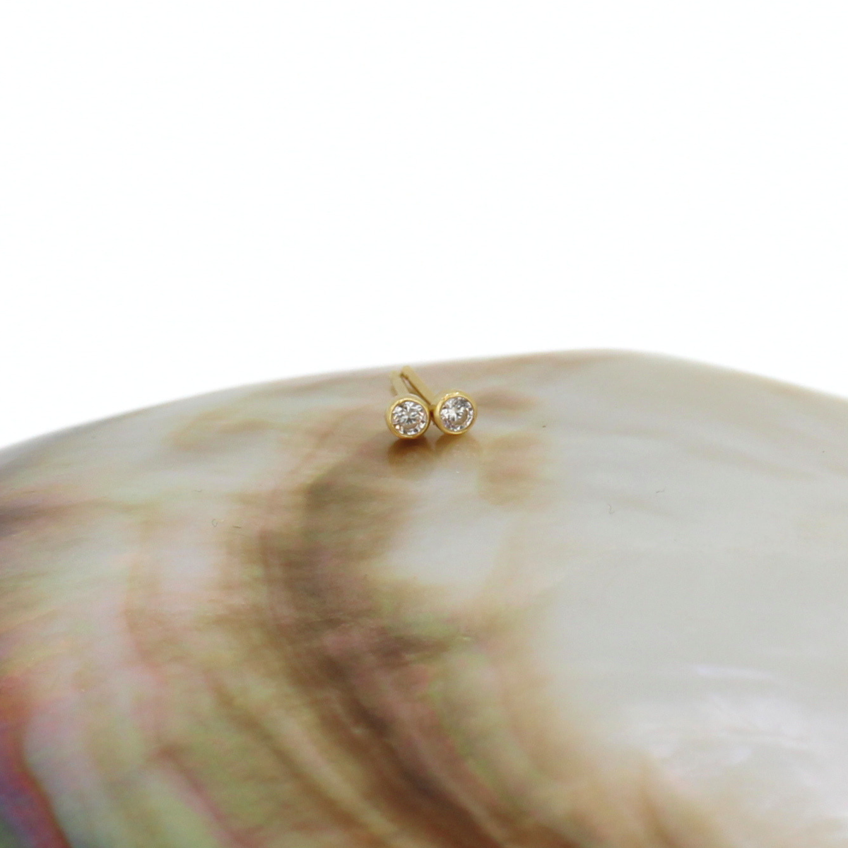 A small gold stud earring set with clear cubic zirconias set on the edge of a large iridescent abalone shell, photographed against a solid white background.