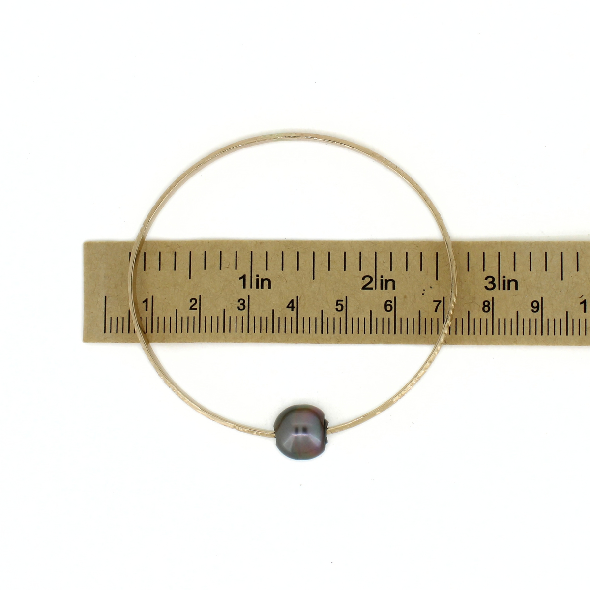 Gold Tahitian pearl bangle bracelet shown over a ruler for size reference 