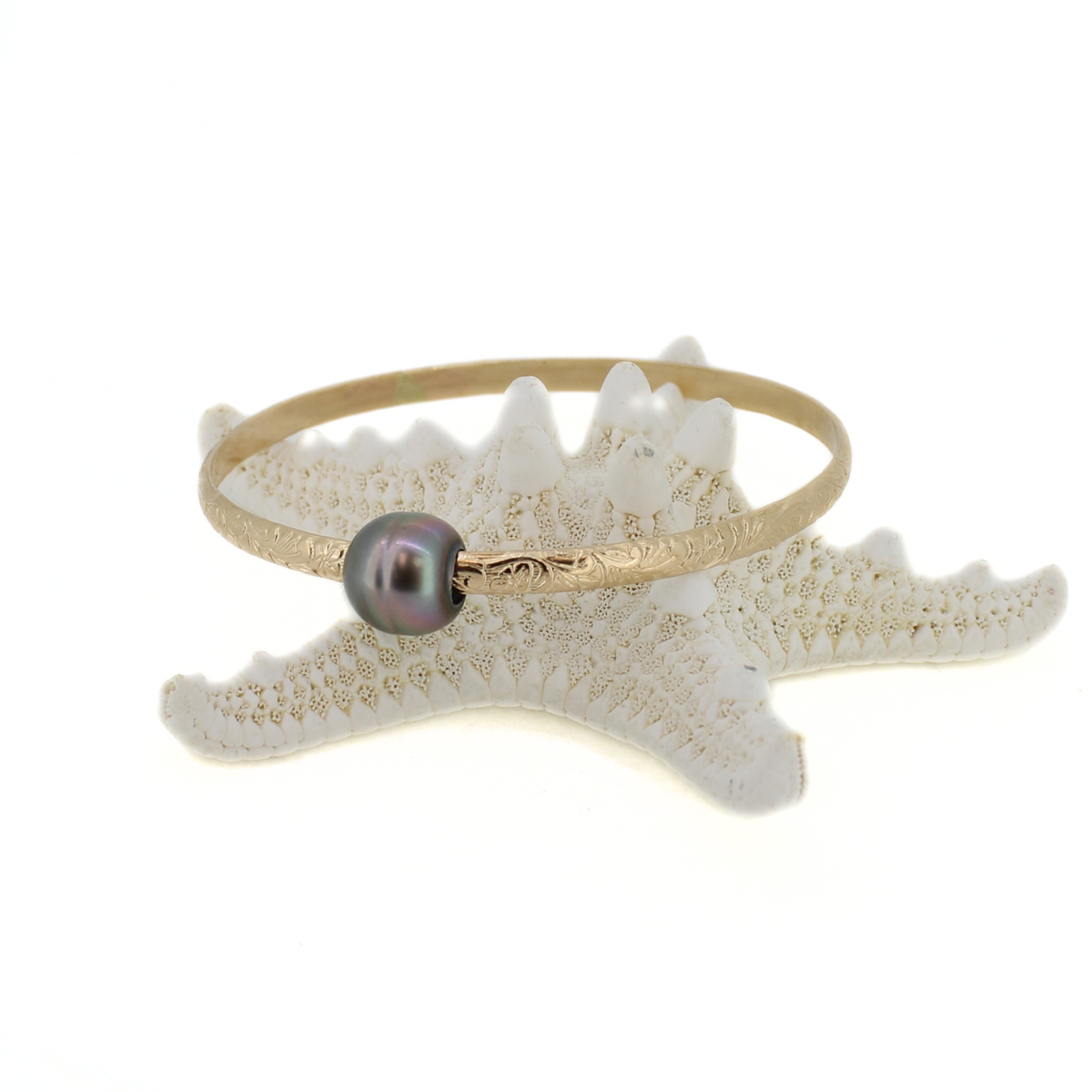 Gold floral printed bangle bracelet with a dark Tahitian pearl displayed on a starfish