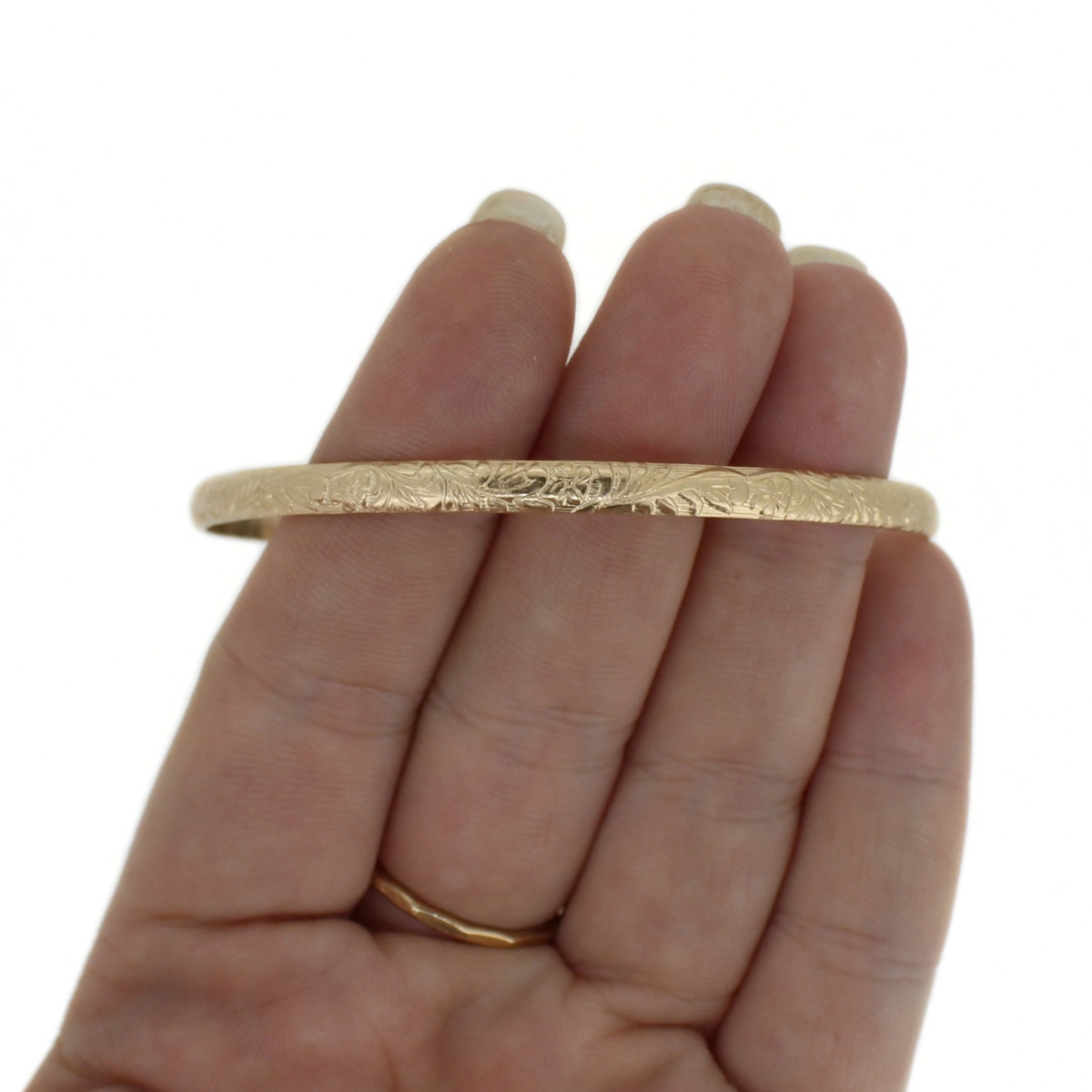 Gold floral printed bangle bracelet displayed on a persons fingers against a white background