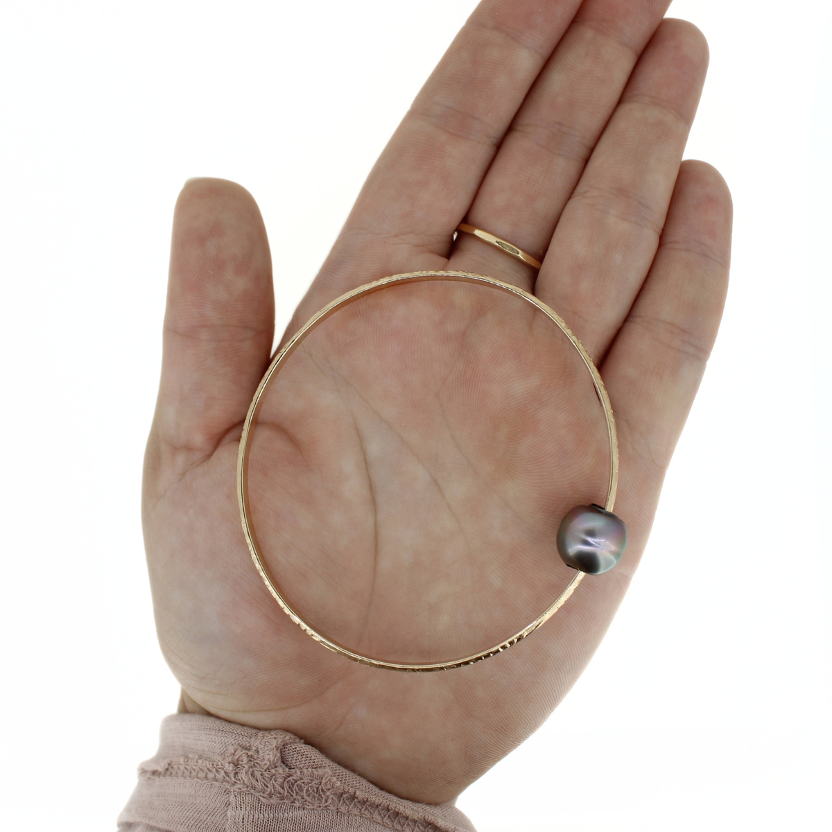 Gold bangle bracelet with a dark gray pearl displayed on an open palm