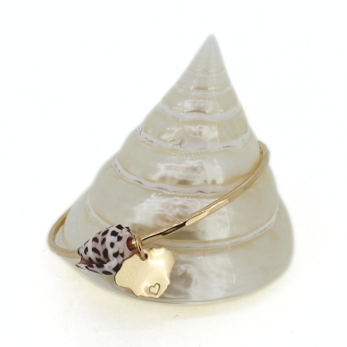 Gold bangle bracelet with cone shell and kauai island charm displayed on a cone shell