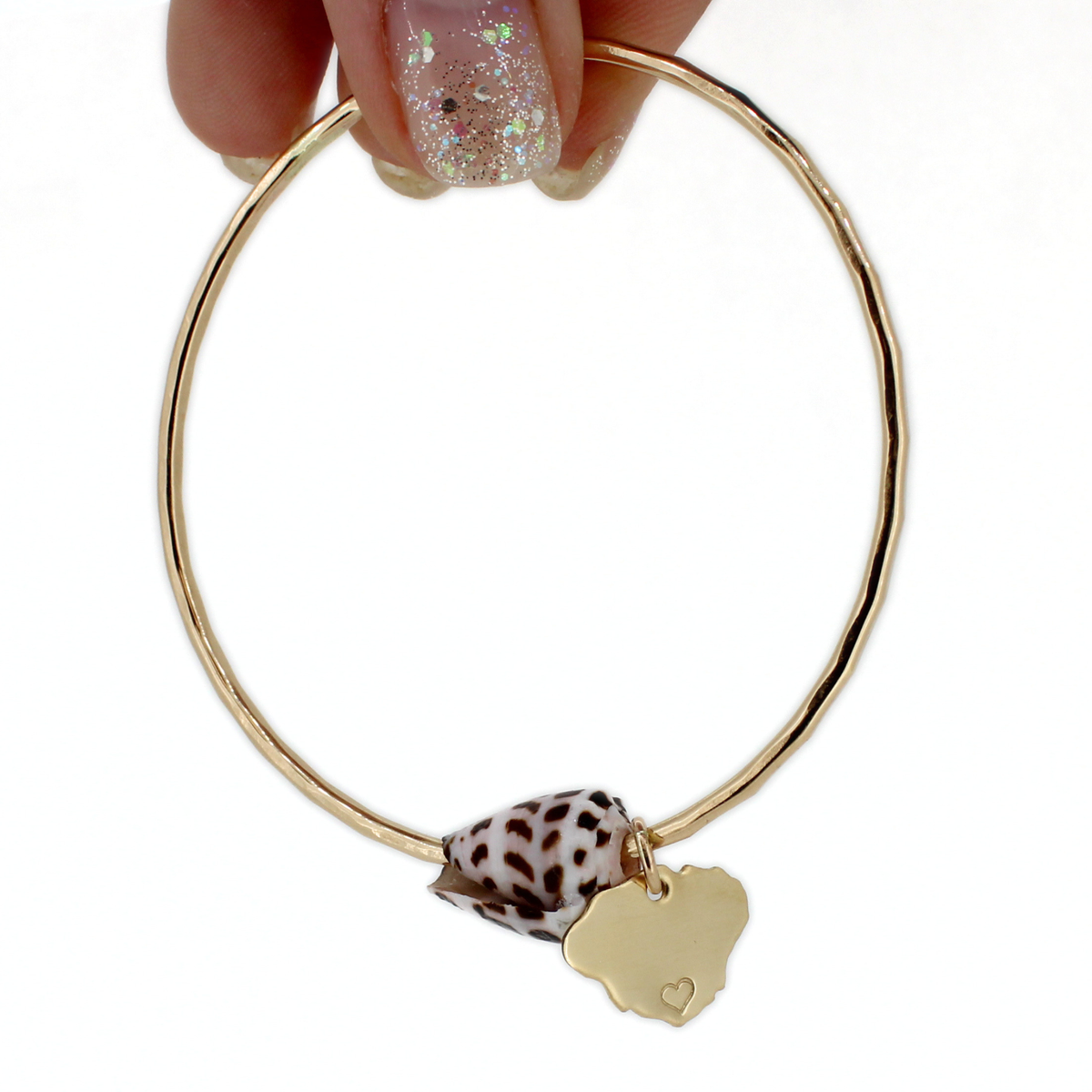 Gold bangle bracelet with cone shell and kauai charm being held against a white background