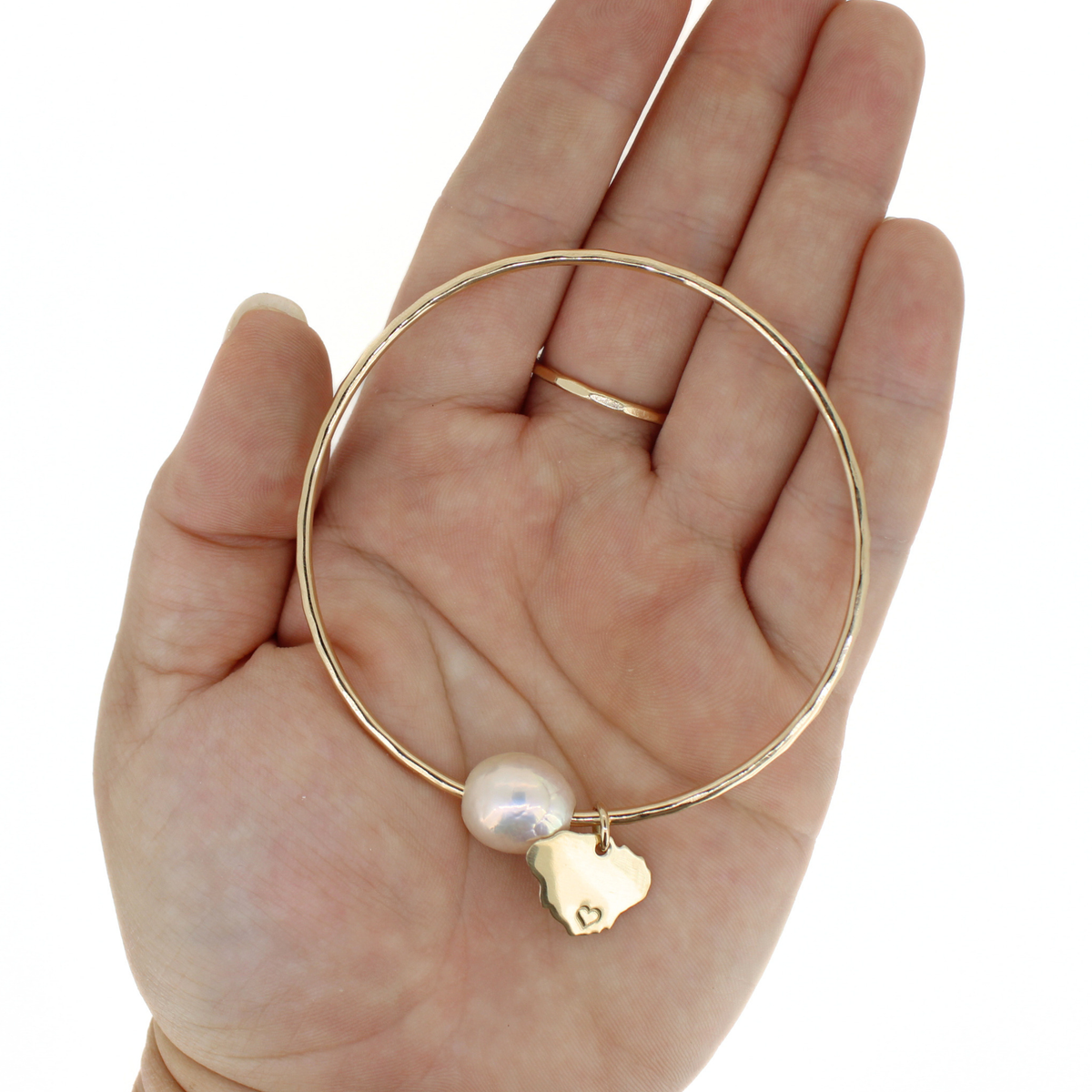 A gold bangle bracelet with a white freshwater pearl and a small gold Kauai charm, displayed on an open hand against a white background.