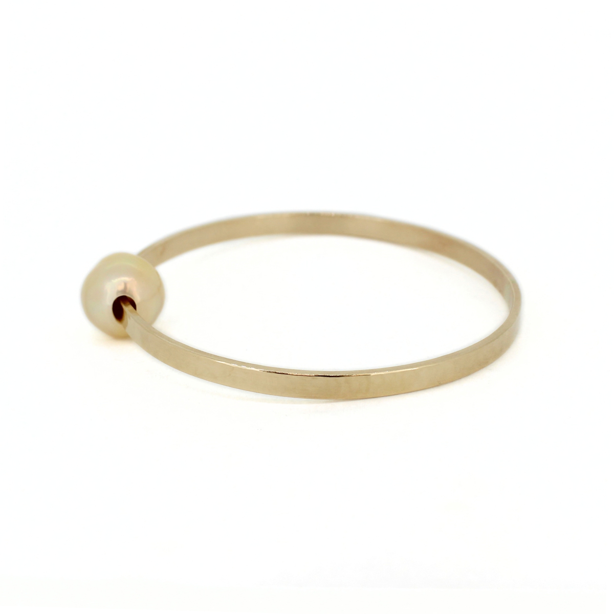 A minimalist gold bangle bracelet with a small, smooth round pearl, shown on a clean white background.