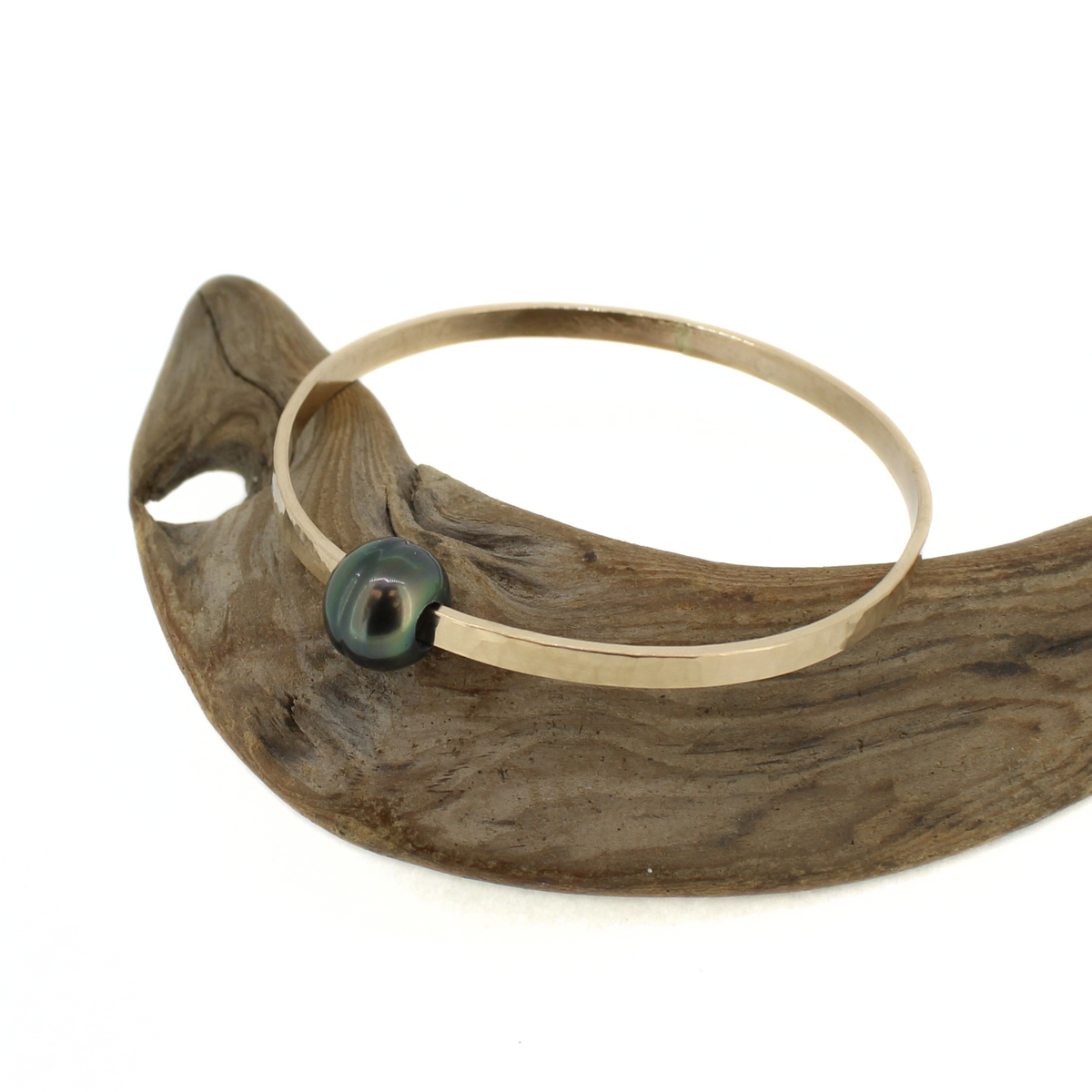 14k gold fill bangle bracelet with a dark Tahitian pearl displayed on a piece of driftwood