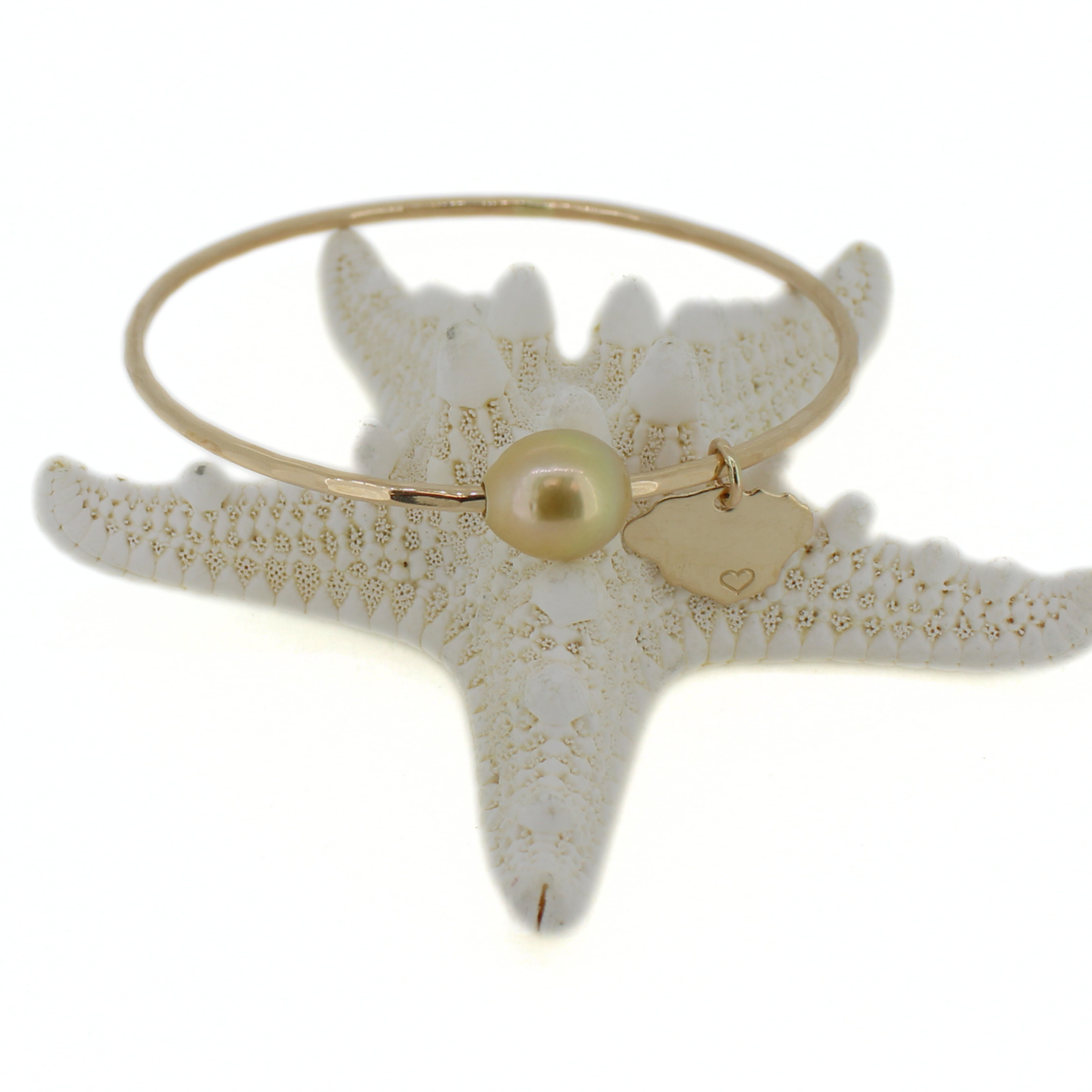 A gold bangle bracelet featuring a  small gold Kauai island charm, and a central gold pearl, displayed on a clean white background.