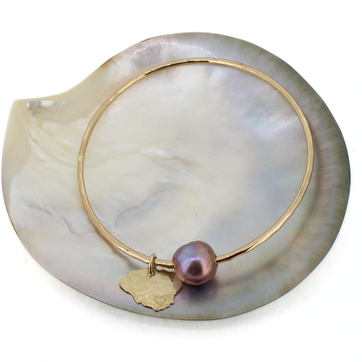 A gold bangle bracelet with a single baroque pearl and a small gold Kauai-shaped charm, displayed on a white mother-of-pearl shell.
