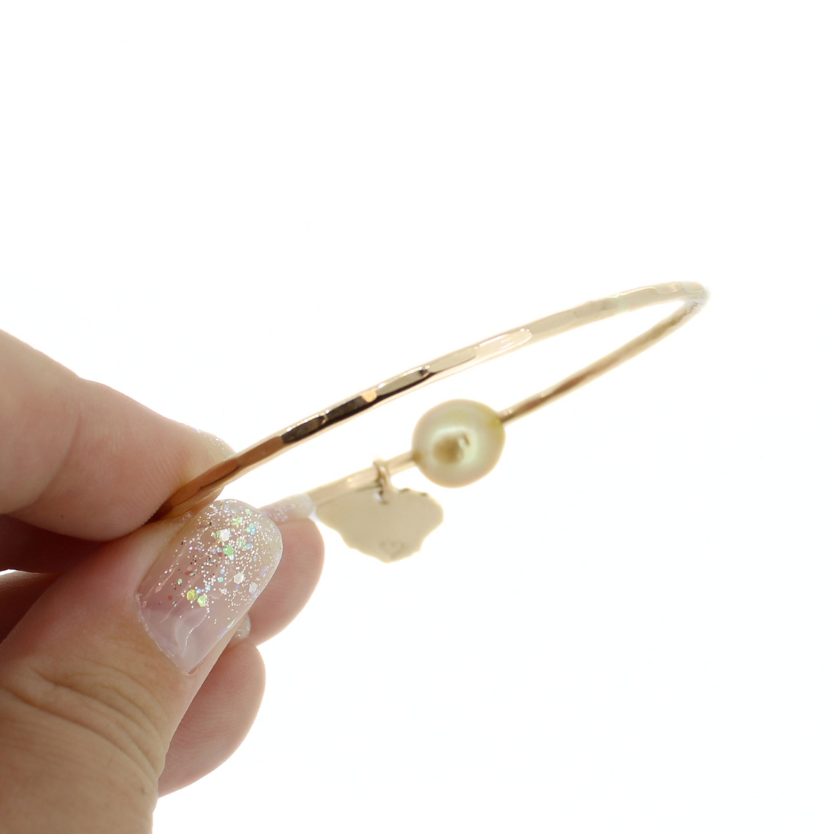 A close-up of a hand holding a thin gold bangle bracelet with a hammered texture, against a plain white background.